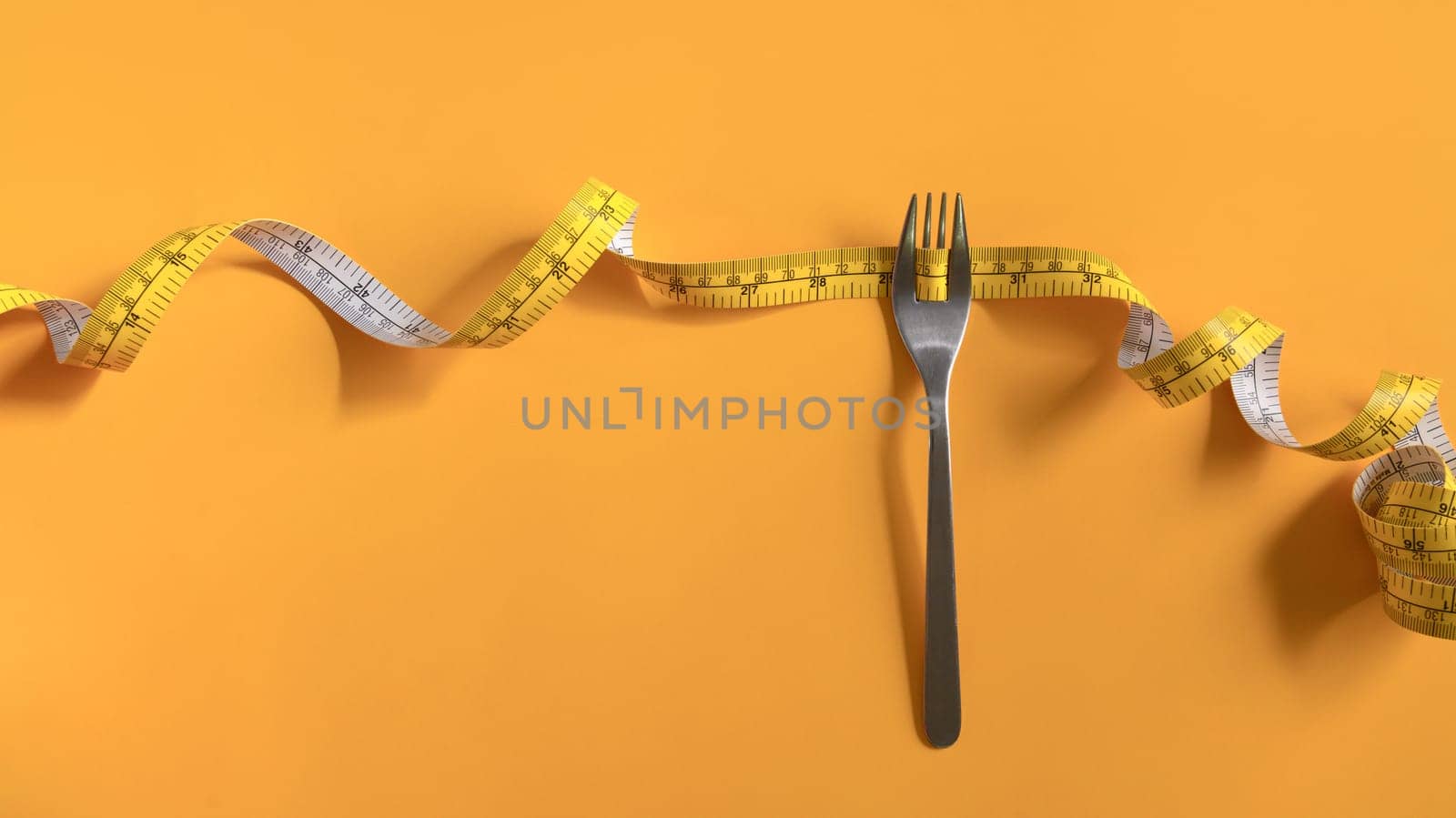 Fork with measuring tape on yellow background. Weight loss and healthy lifestyle concept.