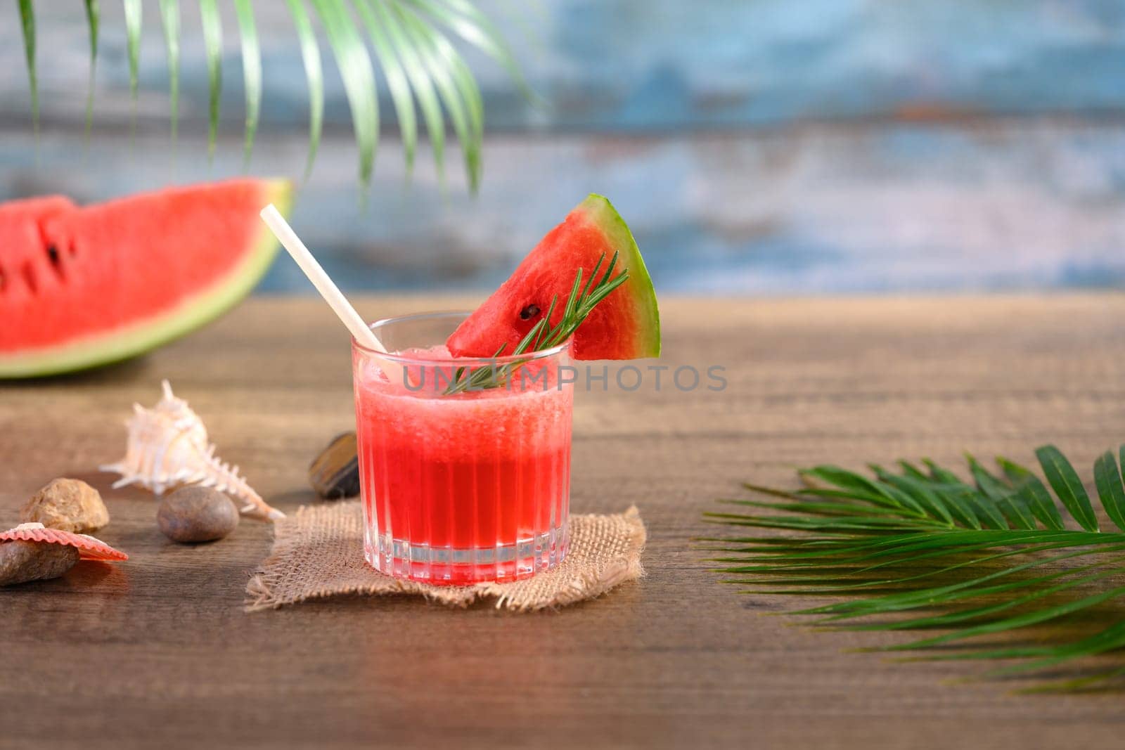 Cold summer fruit drink, fresh watermelon mocktail on wooden table with seashells.