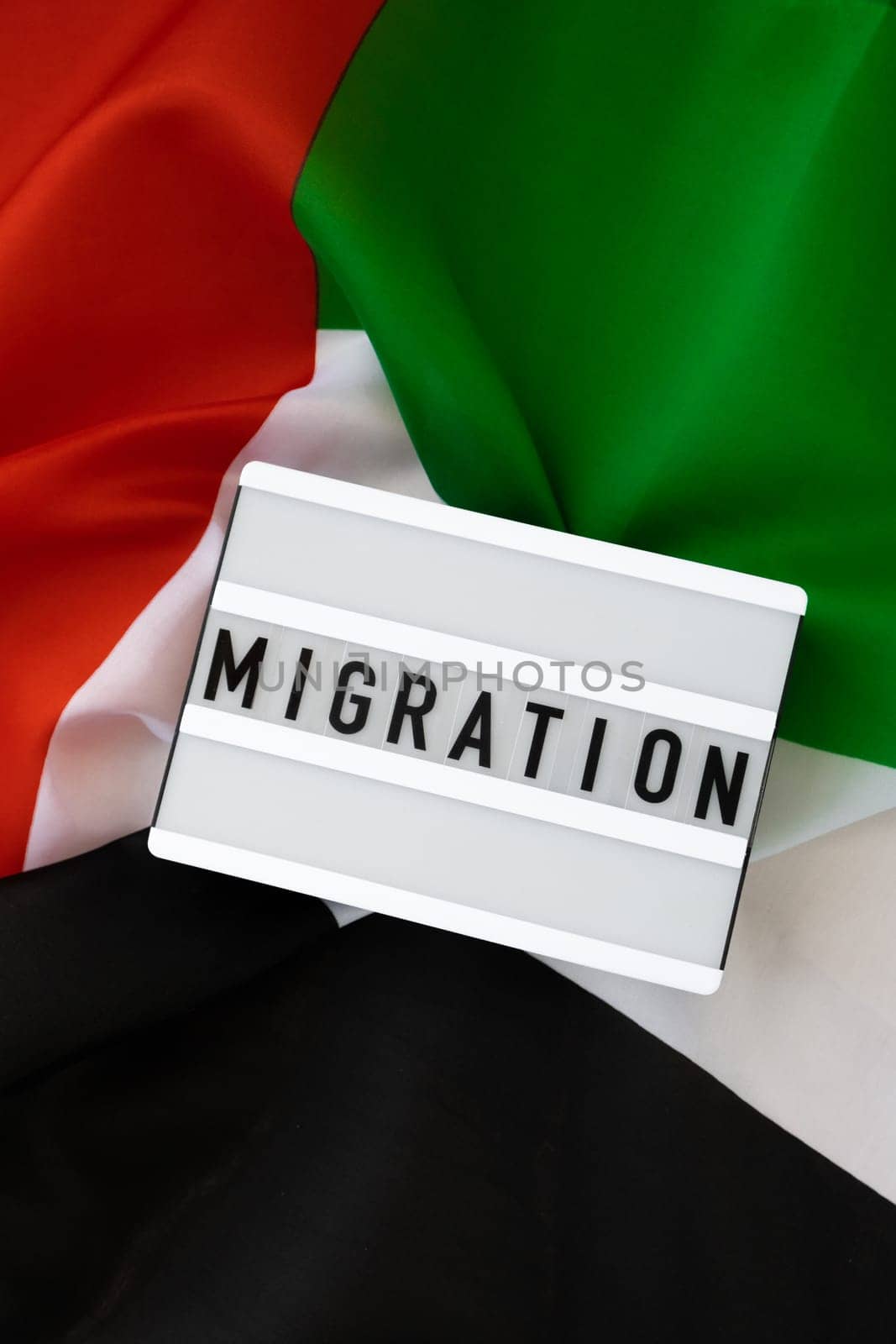 Message MIGRATION on background of UAE flag made from silk. United Arab Emirates national flag with concept of tourism and traveling. Dubai welcoming card. Advertisement
