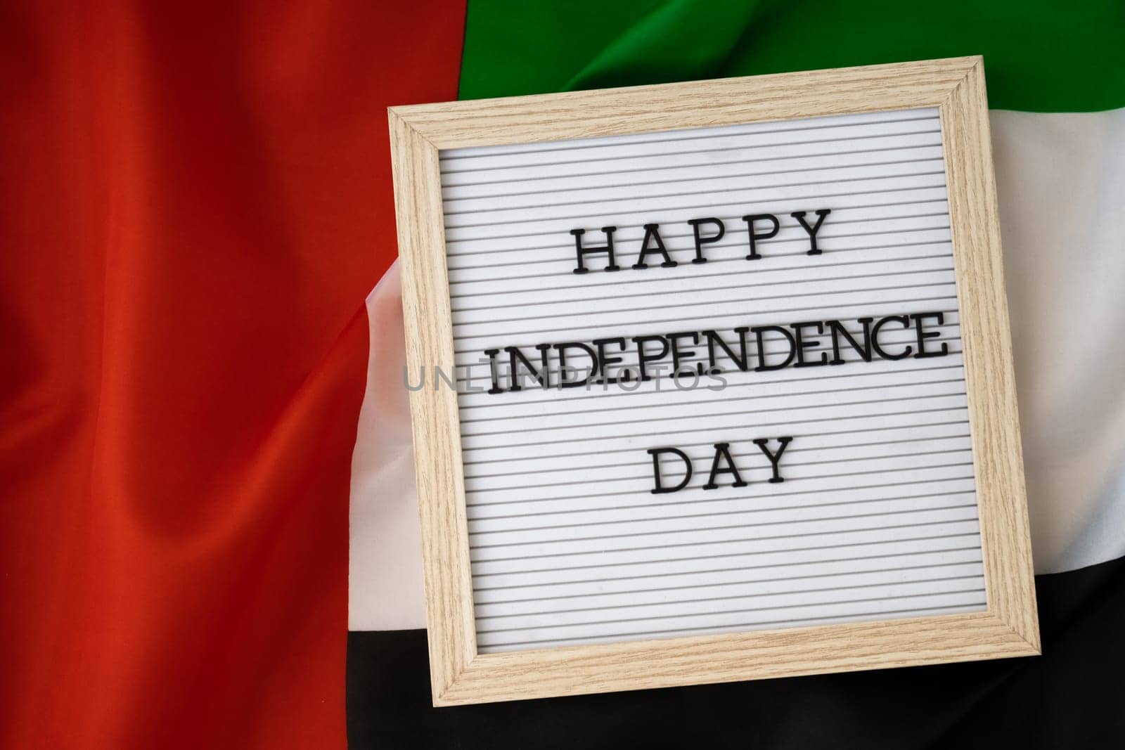 HAPPY INDEPENDENCE DAY text frame on United Arab Emirates waving flag made from silk material. Commemoration Day Muslim Public holiday celebration background. The National Flag of UAE by anna_stasiia