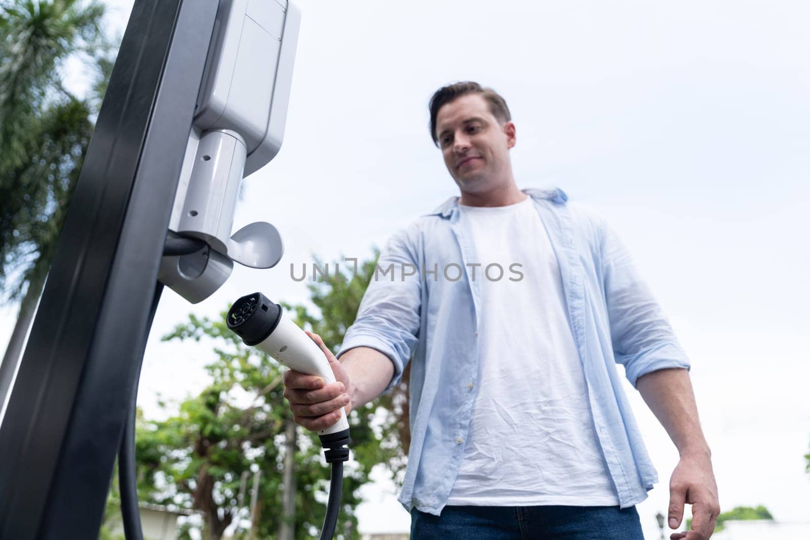 Eco-friendly conscious man recharging modern electric vehicle from EV charging station. EV car technology utilized as alternative transportation for future sustainability. Synchronos
