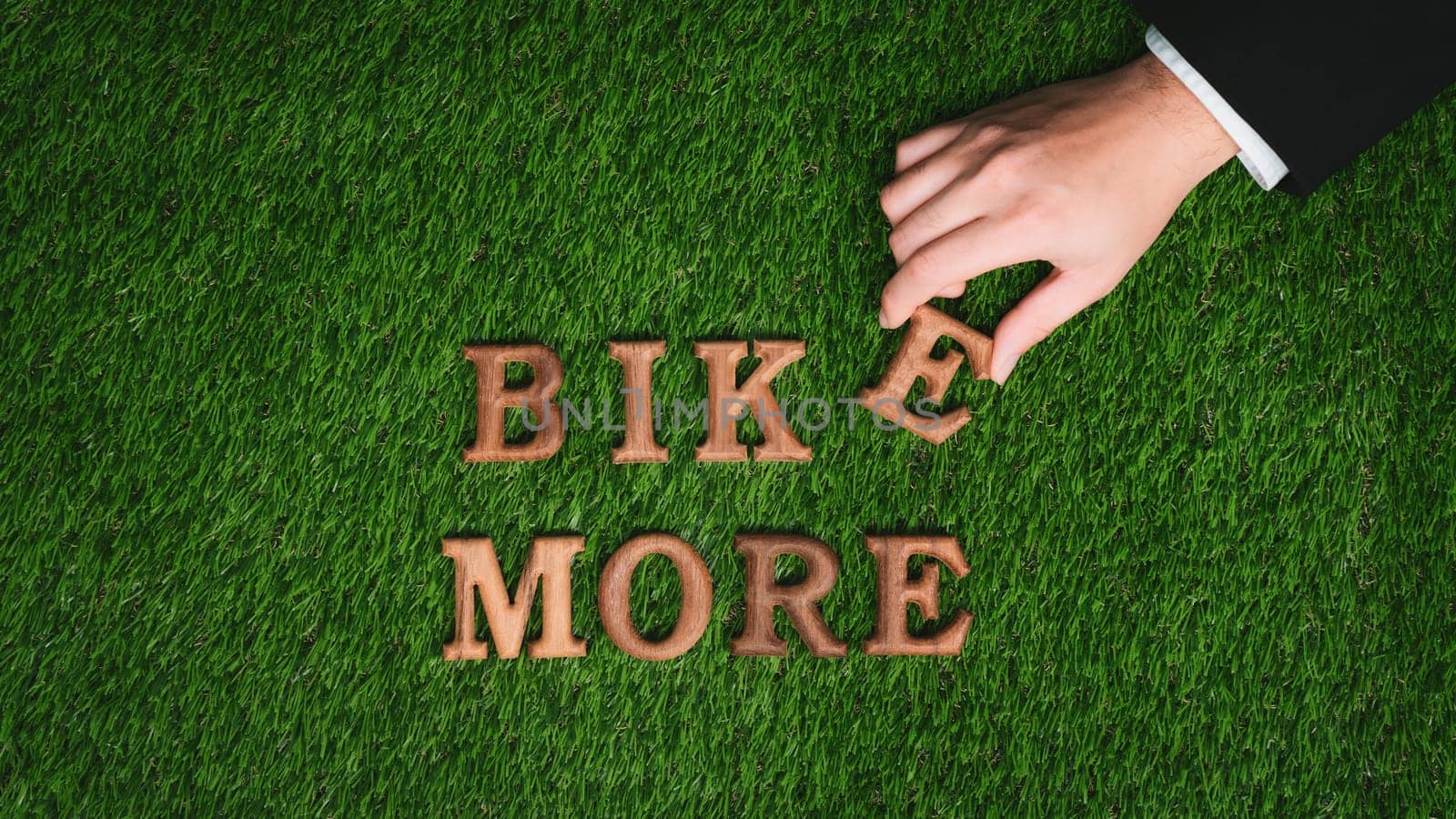 Hand arrange wooden alphabet text in BIKE MORE on green biophilic grass design background as eco symbol for encouraging message for biking campaign and environmental awareness. Gyre