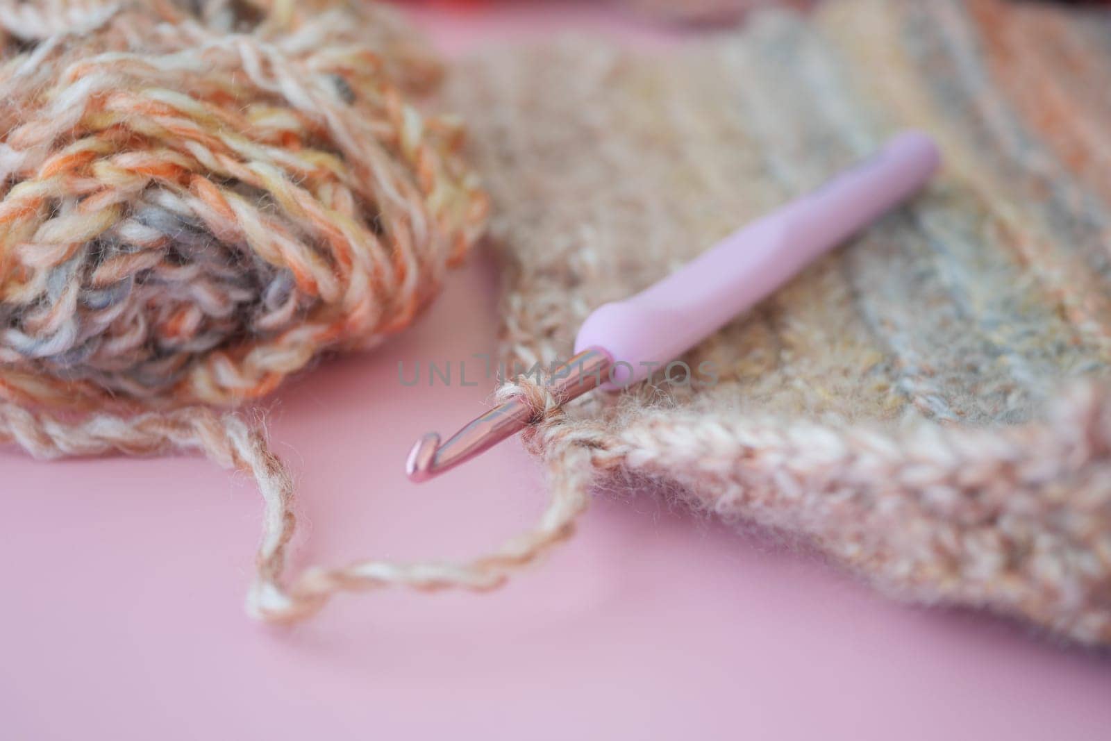 a close up of a crochet hook on a piece of yarn on a pink surface . High quality