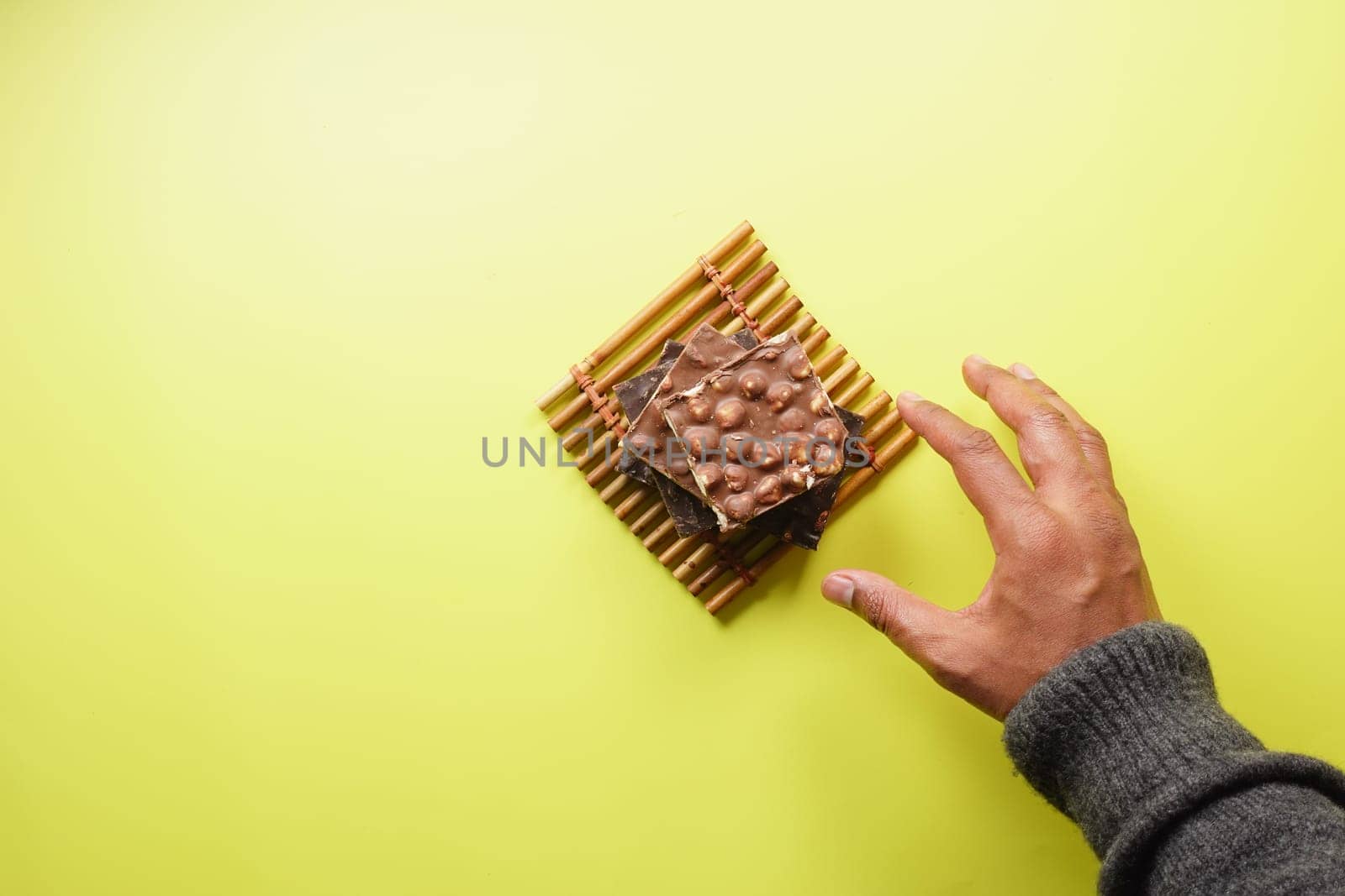 hand reaching for candy with mixed nut on yellow background .