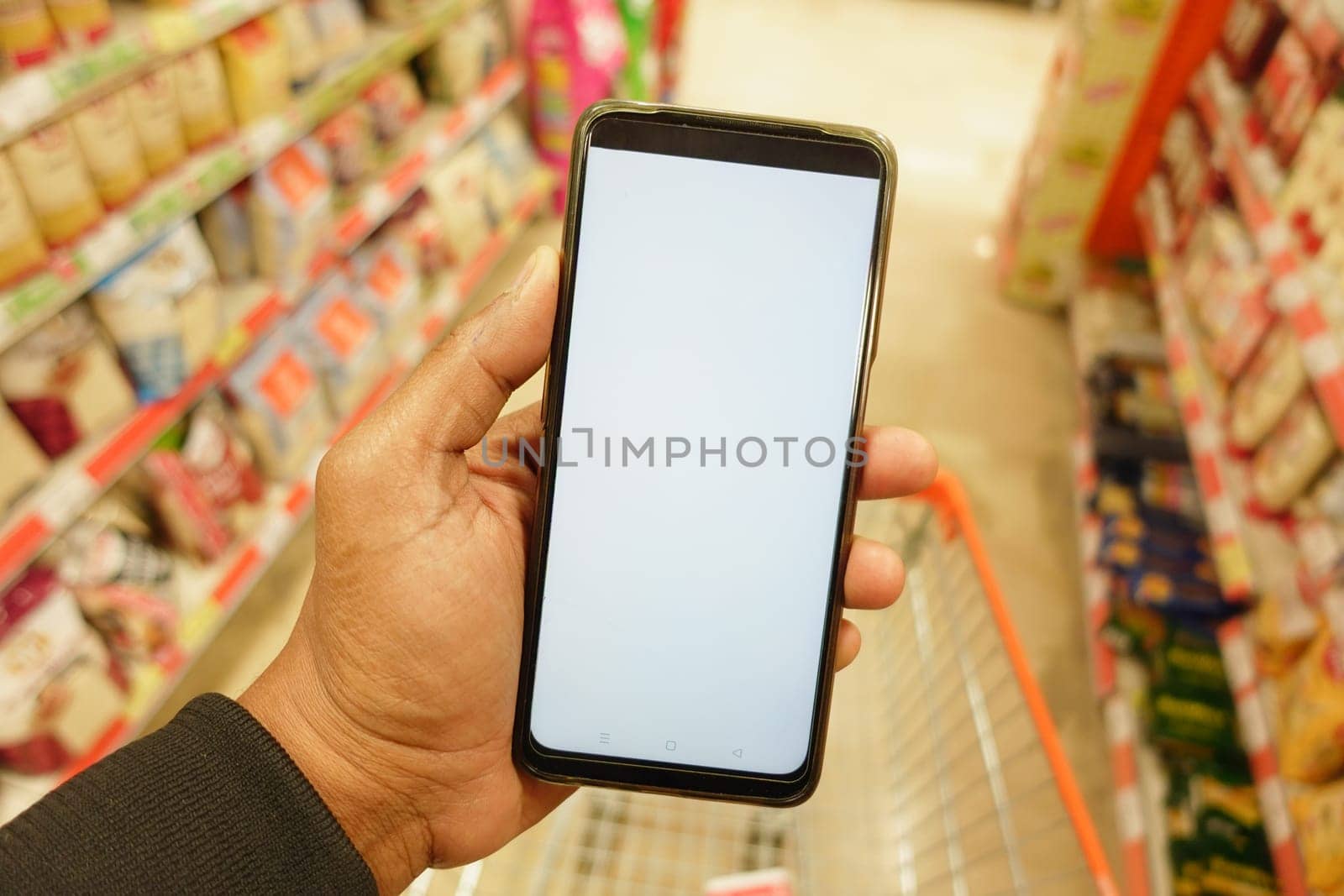 hand holding mobile phone with white screen while shopping at supermarket