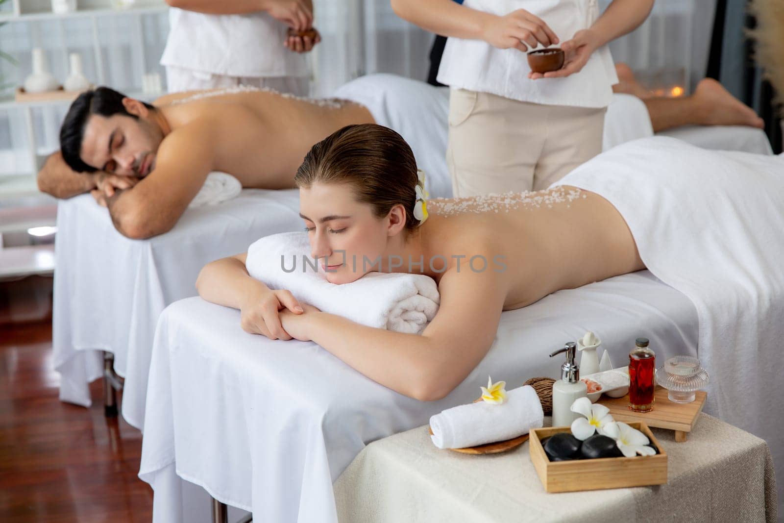 Woman customer having exfoliation treatment in luxury spa salon with warmth candle light ambient. Salt scrub beauty treatment in health spa body scrub. Quiescent