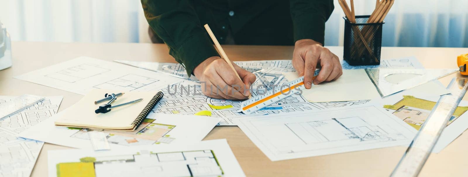 A portrait of architect using divider to measure blueprint. Architect designing house construction on a table at studio, with architectural equipment scattered around. Focus on hand. Delineation