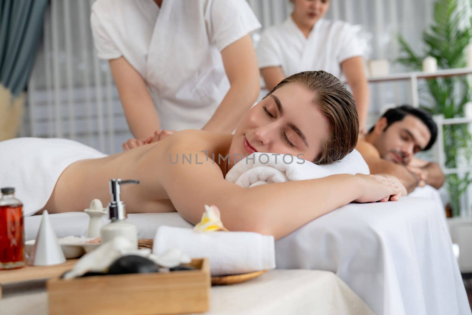 Caucasian couple customer enjoying relaxing anti-stress spa massage and pampering with beauty skin recreation leisure in day light ambient salon spa at luxury resort or hotel. Quiescent