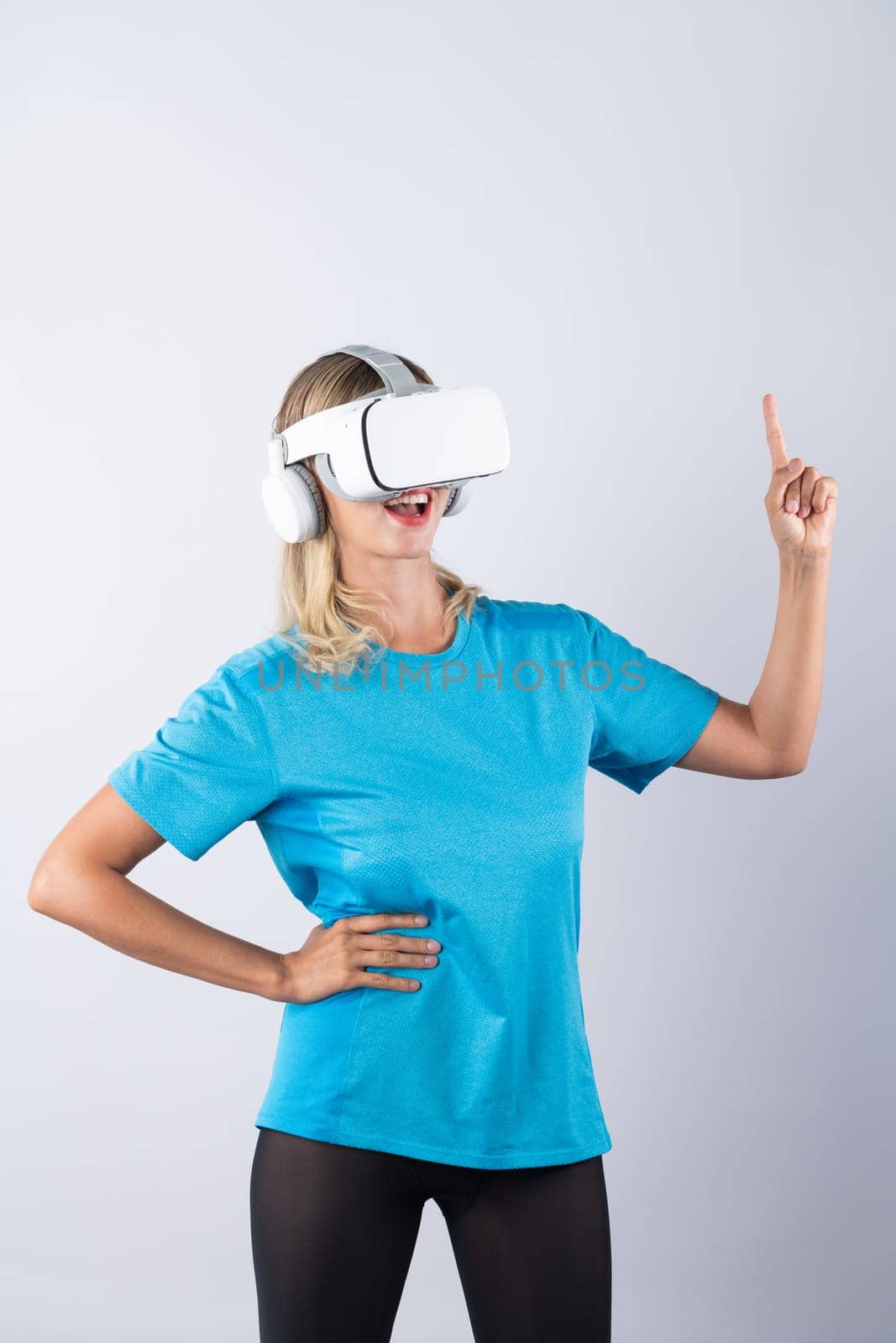 Girl pointing or spinning basketball while using VR glasses. Caucasian woman flexing while wearing casual shirt and visual reality goggles and standing at pink background. Innovation. Contraption.