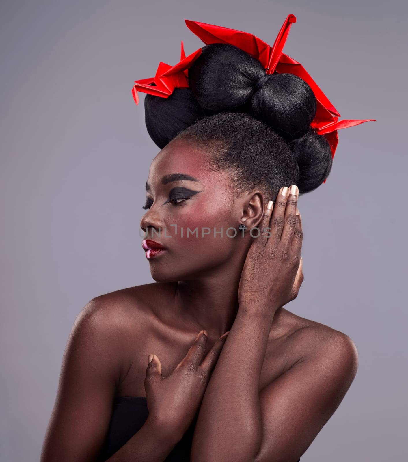 Woman, beauty and origami in studio for cosmetics with red color, Oriental culture and paper bird. African model, bold makeup and grey background for art deco, confidence and creativity with design by YuriArcurs