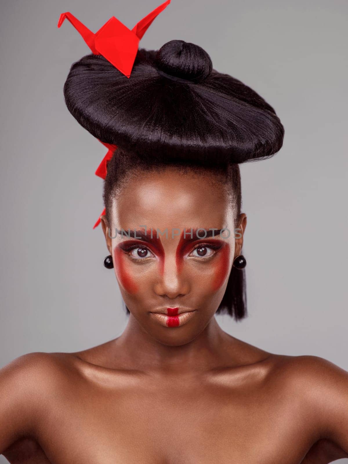 Portrait, makeup and black woman with origami for beauty in studio isolated on gray background. Face, creative cosmetics and confident model with red paper bird in hair, skincare and Japanese art by YuriArcurs