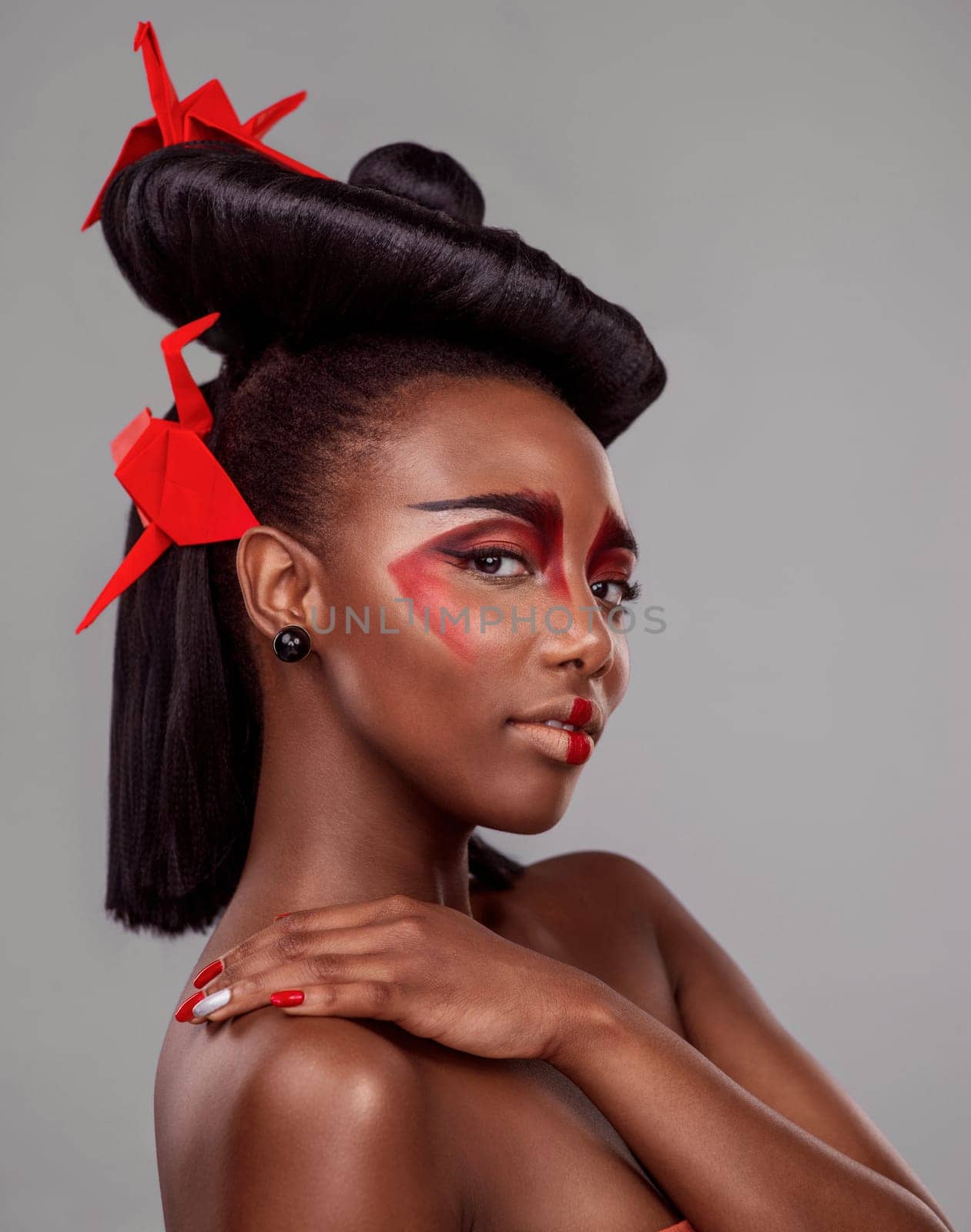 Portrait, makeup and beauty of black woman with origami in studio isolated on gray background or backdrop. Face, creative cosmetics and confident model with red paper crane in hair, skincare and art.