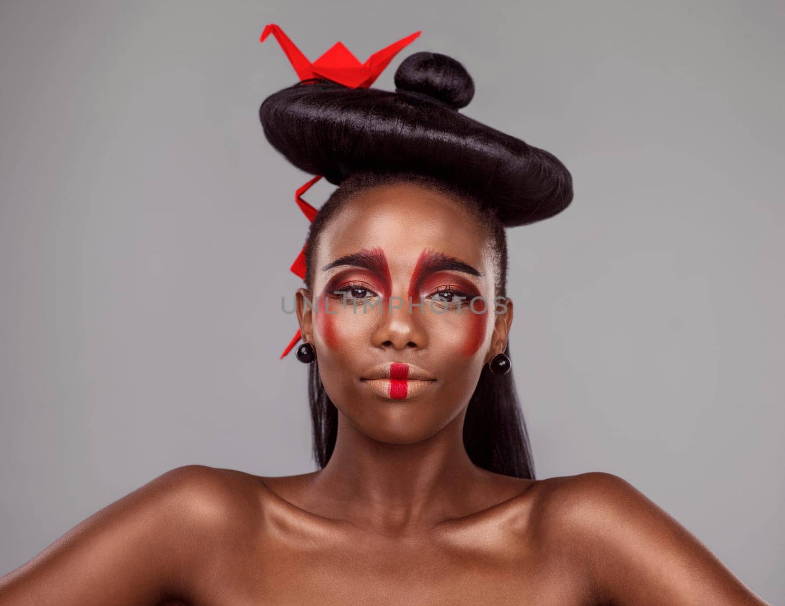 Portrait, makeup and black woman with origami for art in studio isolated on gray background. Face, creative cosmetics and confident serious model with red paper crane in hair, skincare and beauty.