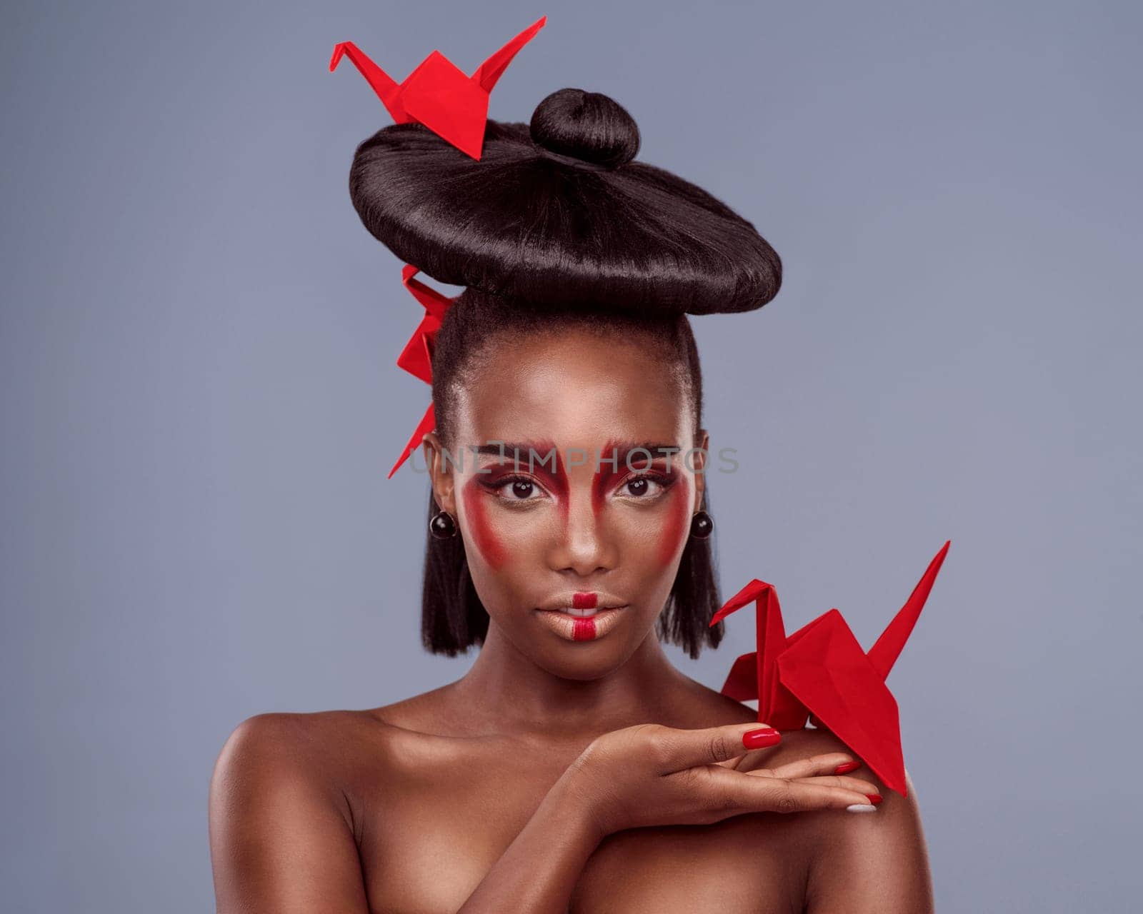 Portrait, cosmetics and black woman with origami for art, beauty or skin in studio isolated on gray background. Face, creative makeup and confident or serious model with oriental paper crane in hair by YuriArcurs