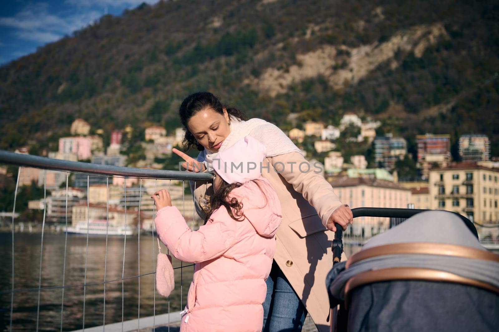 Young pretty woman mother and kids walking together in the city of Como, admiring the lake while walking along the promenade on a sunny winter day