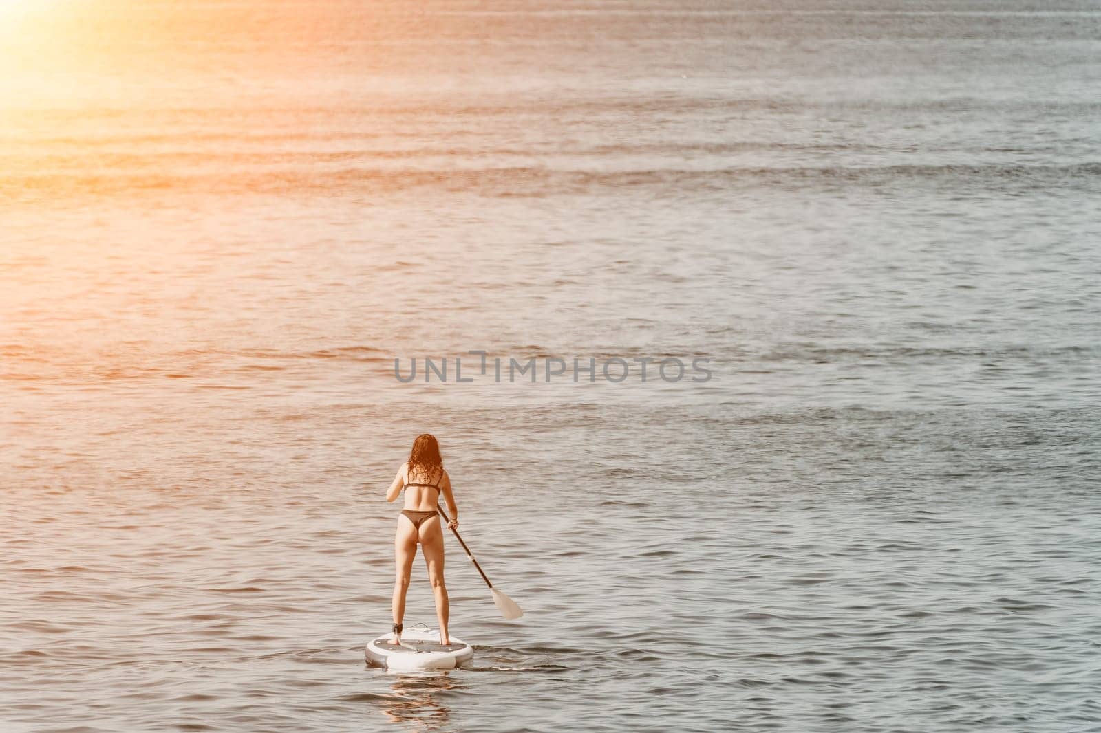 Sea woman sup. A happy positive woman in hat with family relaxing in sea, aerial back view of family on SUP board floating on calm water. Active lifestyle at sea. Summer vacation. Slow motion