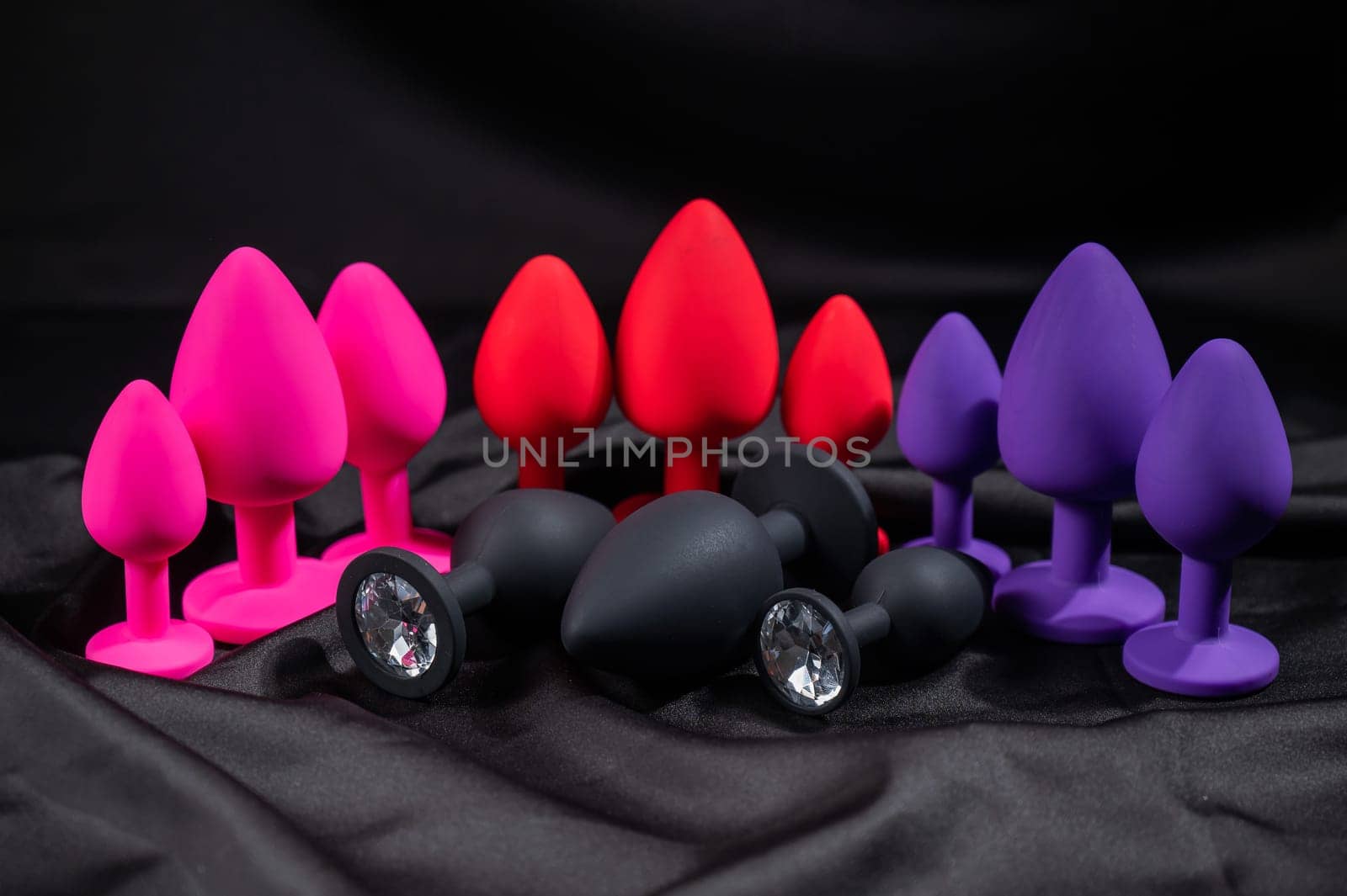 A set of silicone anal plugs in different colors and sizes on a black silk sheet