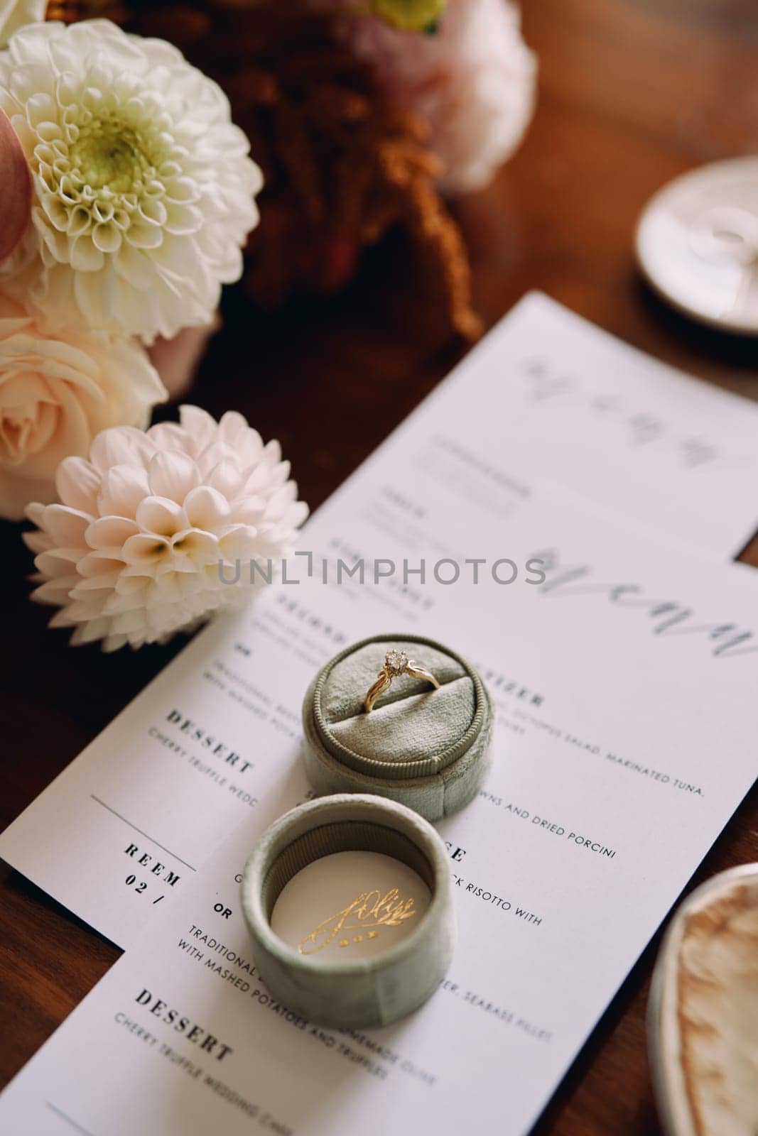 Engagement ring in a box lies on a holiday menu near flowers by Nadtochiy