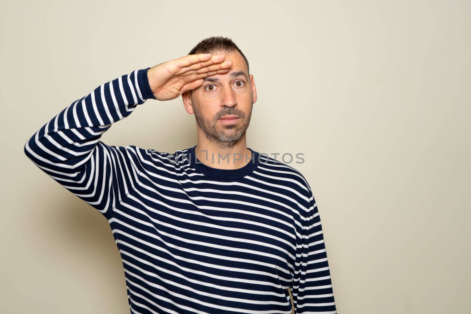 Hispanic man in his 40s saluting the camera with a military salute in an act of honor and patriotism, showing respect. Isolated on beige background. by Barriolo82