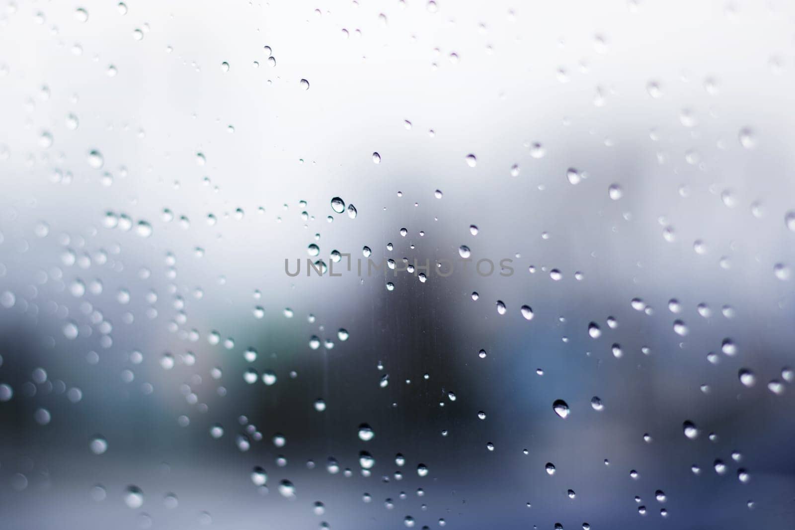 Water droplets cascade down a glass window, creating a blurry backdrop of tints and shades. The sky is painted in electric blue, capturing the beauty of liquid drizzle and moisture