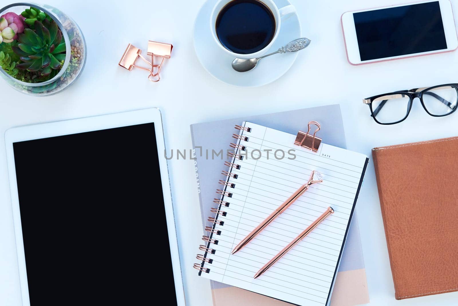 Tablet, notebook and coffee on desk with phone for working, writing notes and planning for career. Creative workplace, business and diary, digital tech and stationery on blue background for job.