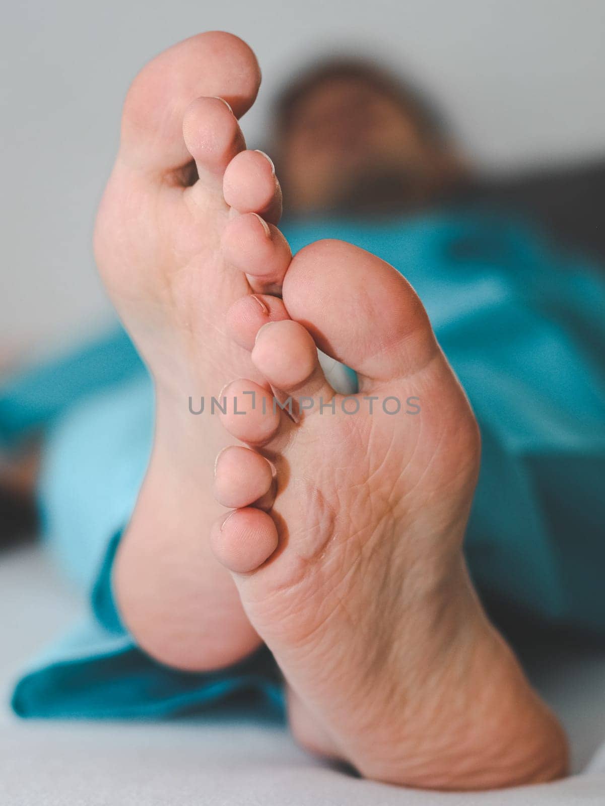 Clean and splayed feet of a young caucasian male patient lying on a bed by Nataliya