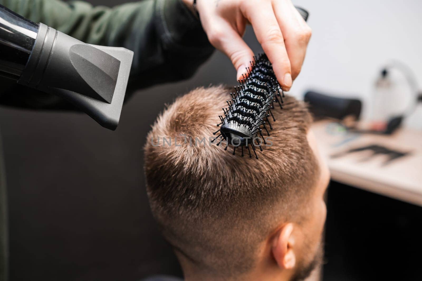 Barber brushes man short hair using dryer in barbershop by vladimka