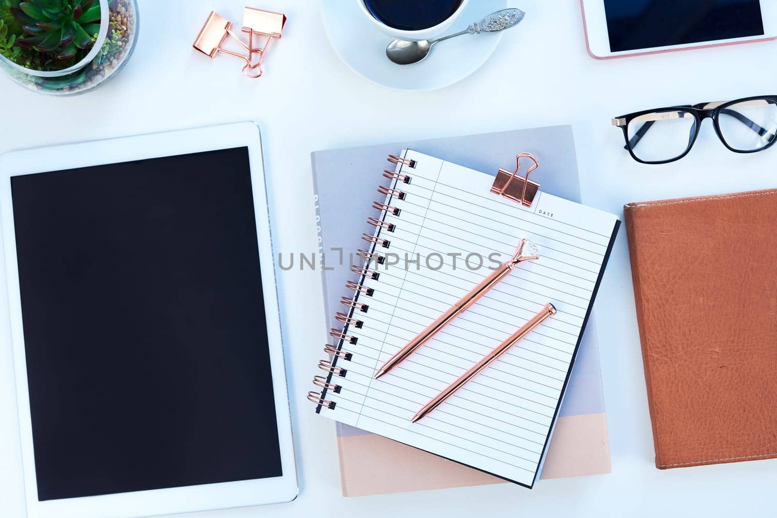 Tablet, diary and coffee on desk in studio for working, writing notes and planning for career. Creative workplace, business and notebook, digital tech and stationery on blue background for job.