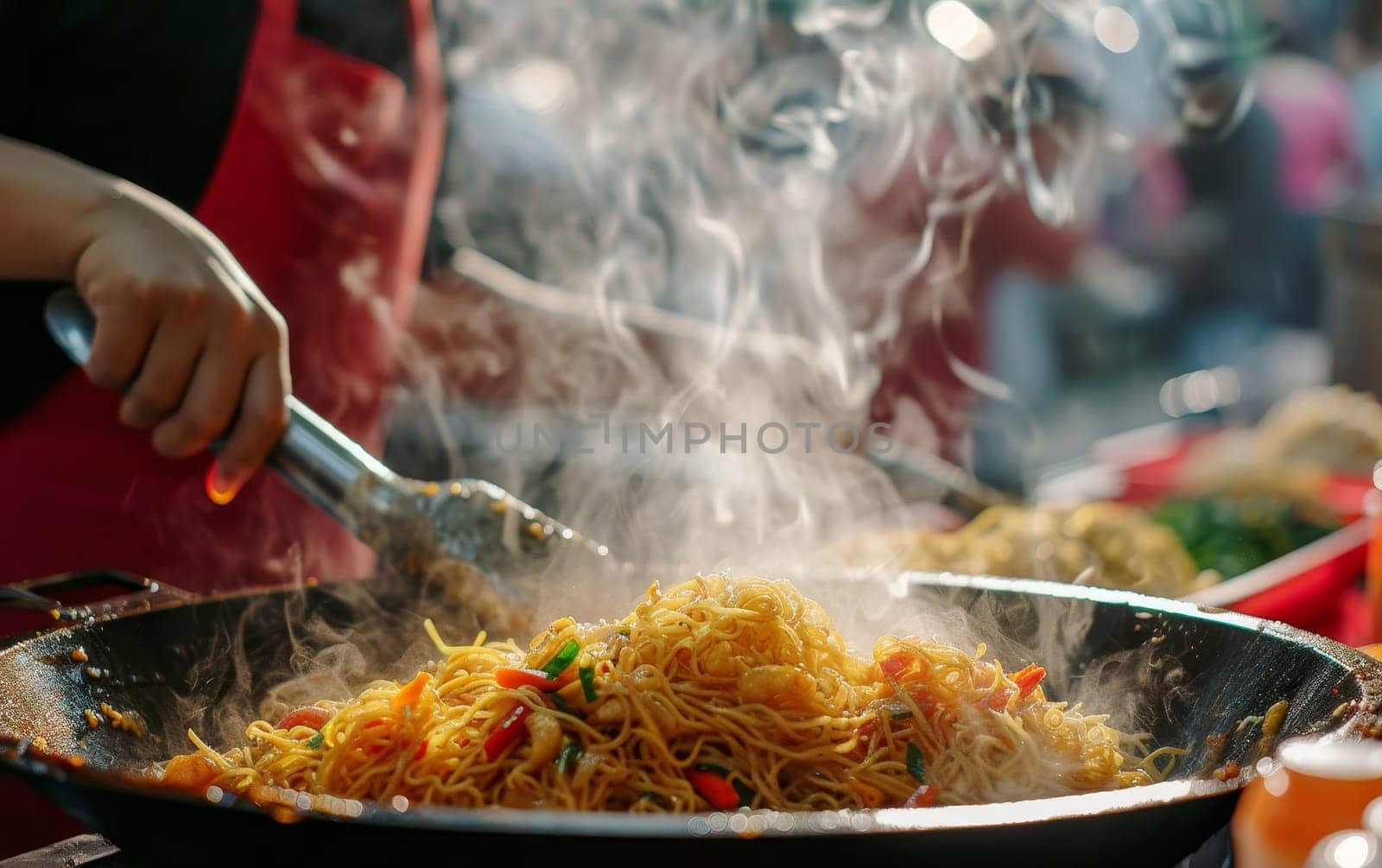 Steam rises from a sizzling wok as noodles are expertly tossed at a bustling street food market stall