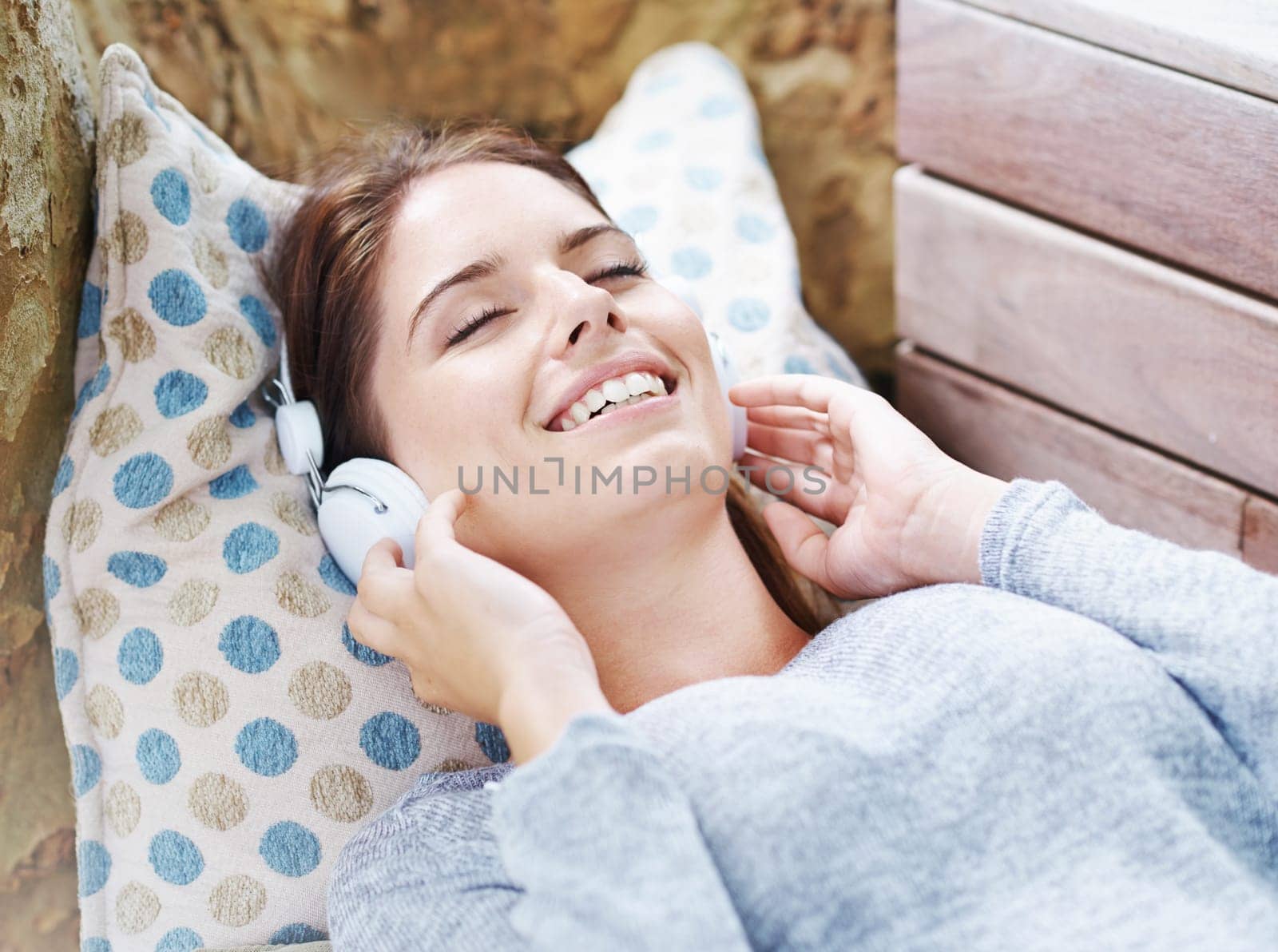 Cheerful, woman and headphones and listening with music, podcast or audio on couch in backyard. Female person, smile and happy at home in outdoor in relax, free and peace with tech for streaming.