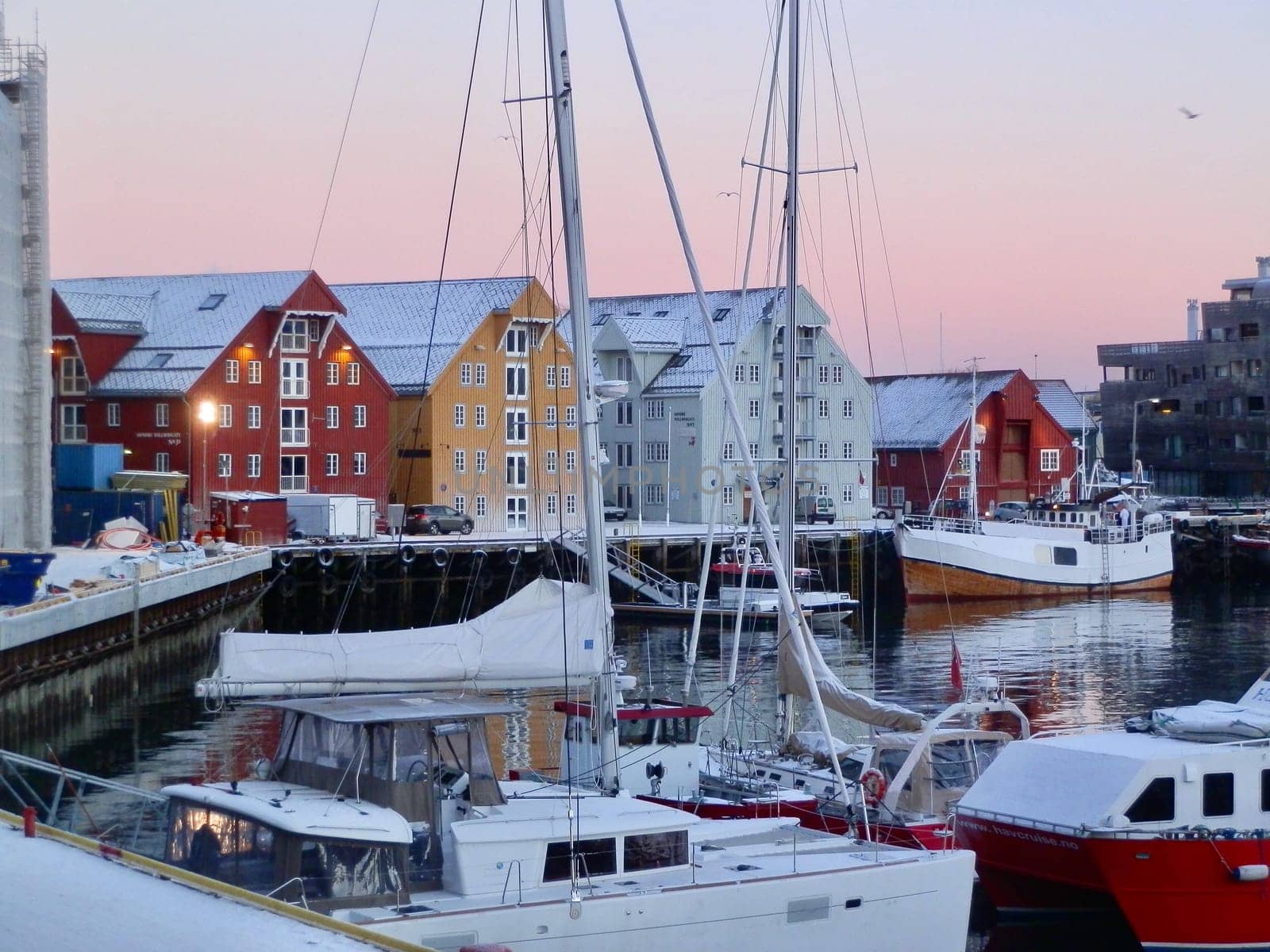 A beautiful pink sky is the backdrop for the harbor at Tromso at dawn, where red is a color of choice for buildings as well as boats.
