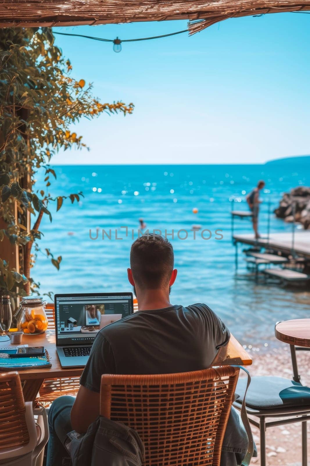 Person working on a laptop at a seaside cafe, enjoying the sunny atmosphere and calming ocean sounds