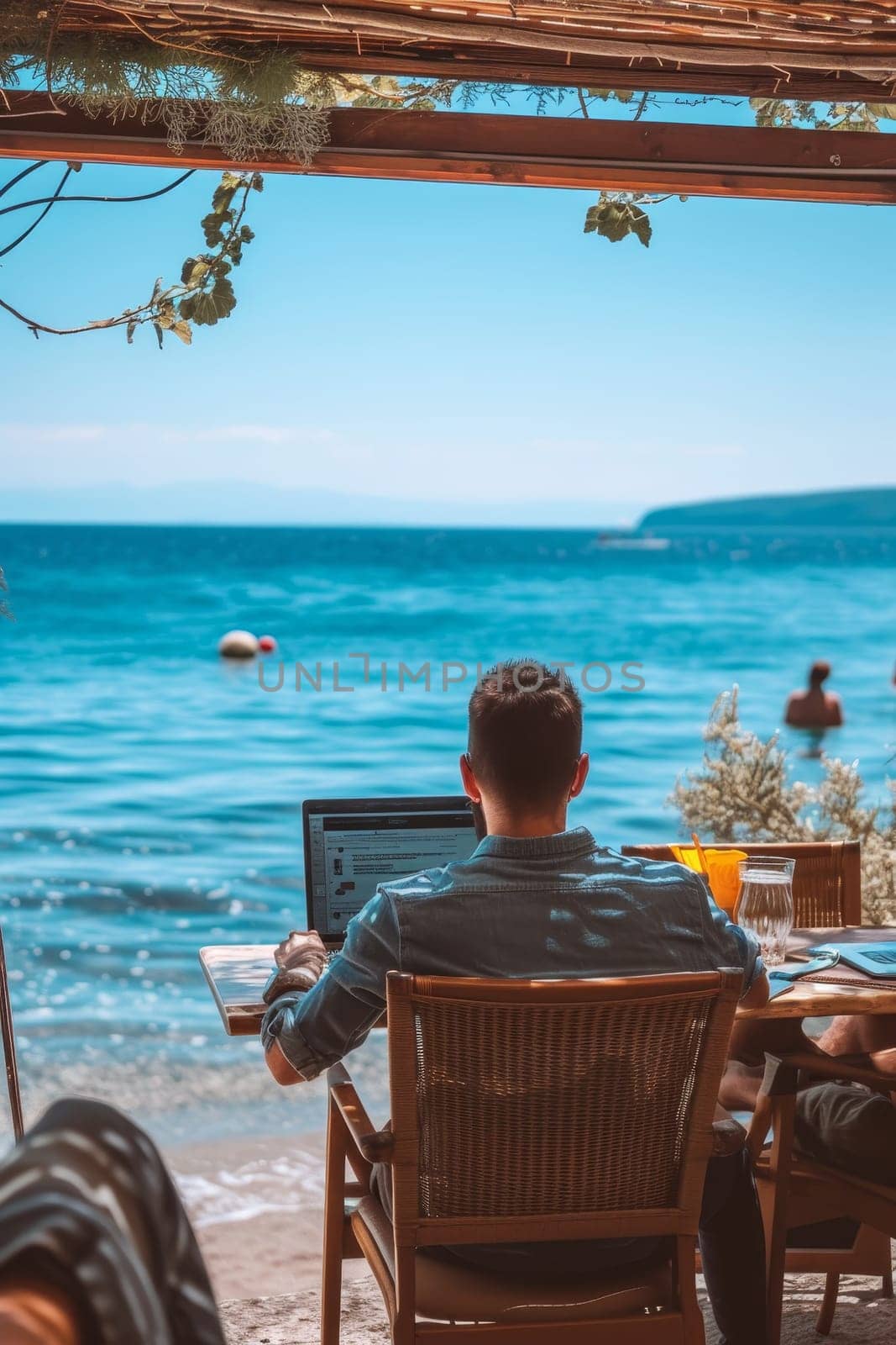 Person working on a laptop at a seaside cafe, enjoying the sunny atmosphere and calming ocean sounds