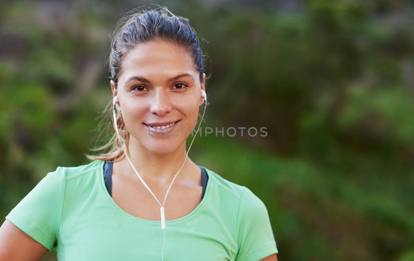 Runner, portrait and happy woman listening to music for exercise or workout in park, woods or forest. Athlete, fitness and girl training in summer and streaming audio with resilience for challenge by YuriArcurs