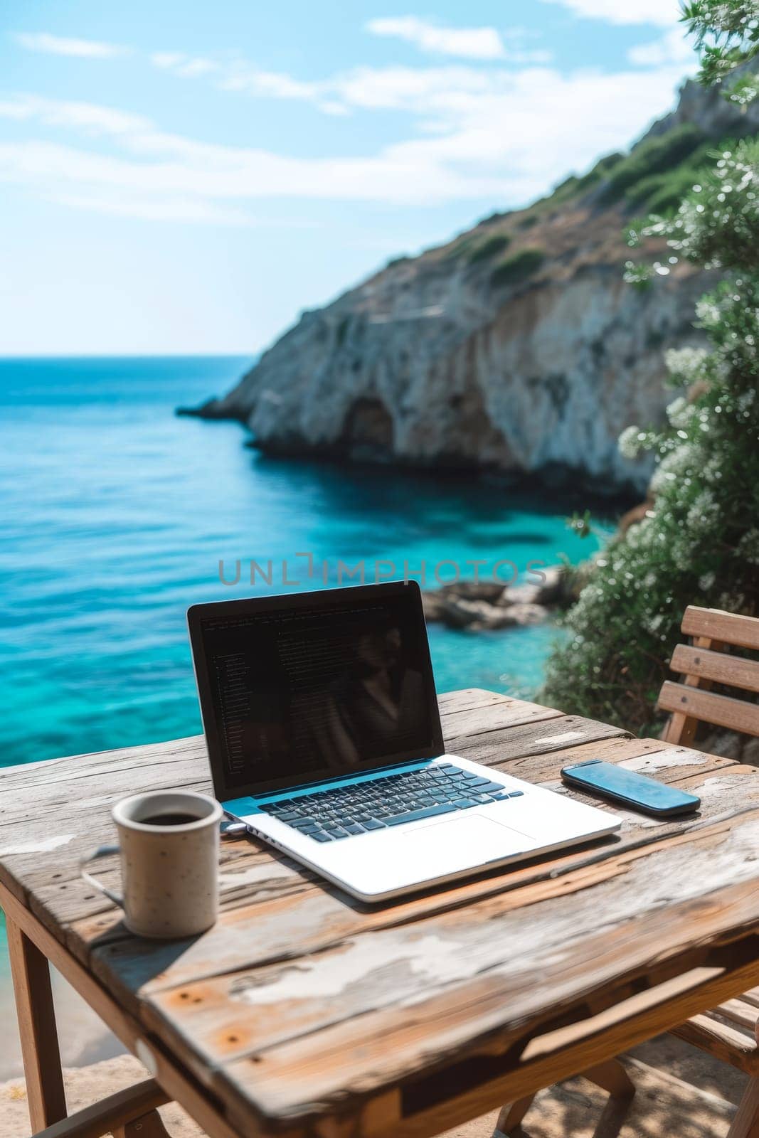 Laptop set up on a wooden table with a breathtaking view of the sea and cliffside