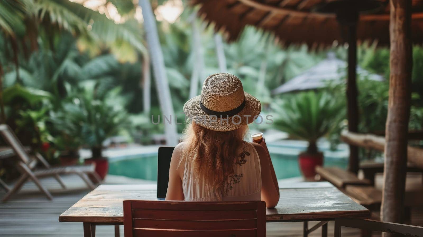 Back view of a relaxed woman with a hat, sipping coffee and overlooking a lush tropical landscape