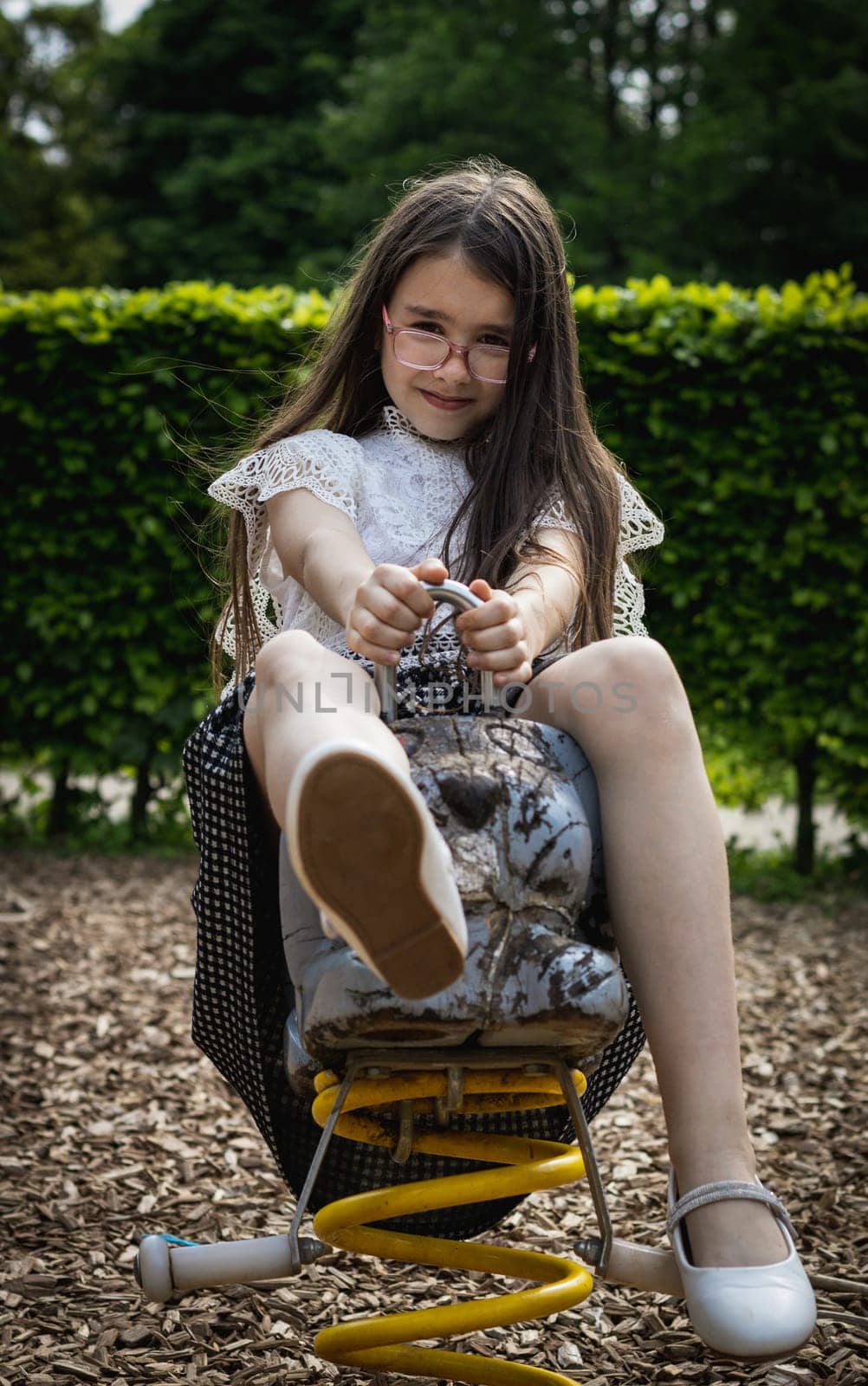Happy girl rides on a spring wooden swing in the park. by Nataliya
