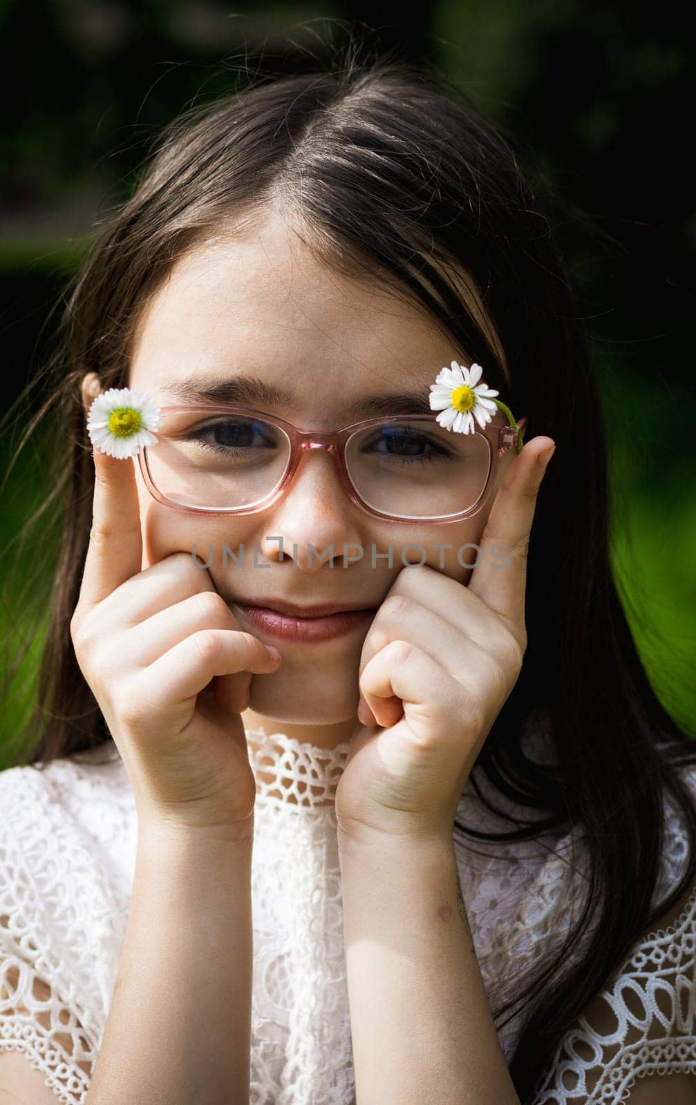 Portrait of one beautiful brunette caucasian girl in glasses holding meadow daisies in the frame with her hands, standing in the park on a summer day.