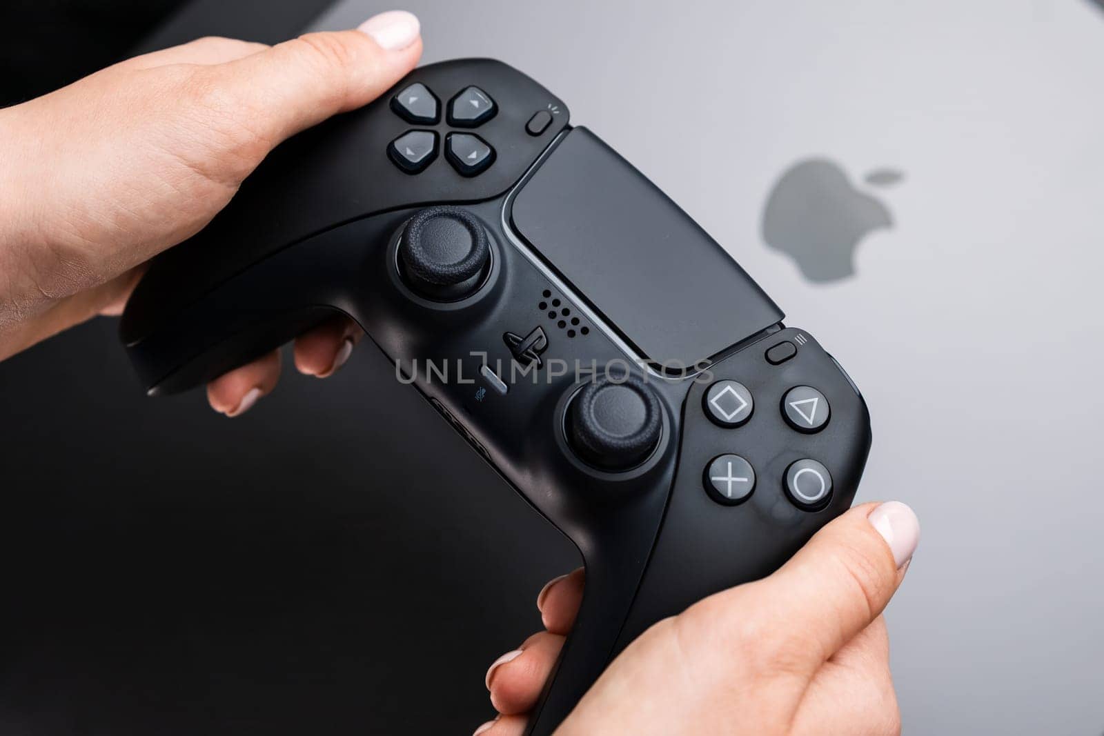 BERLIN , GERMANY - FEBRUARY 14 2024: Womans hands holding video game controller over MacBook Pro