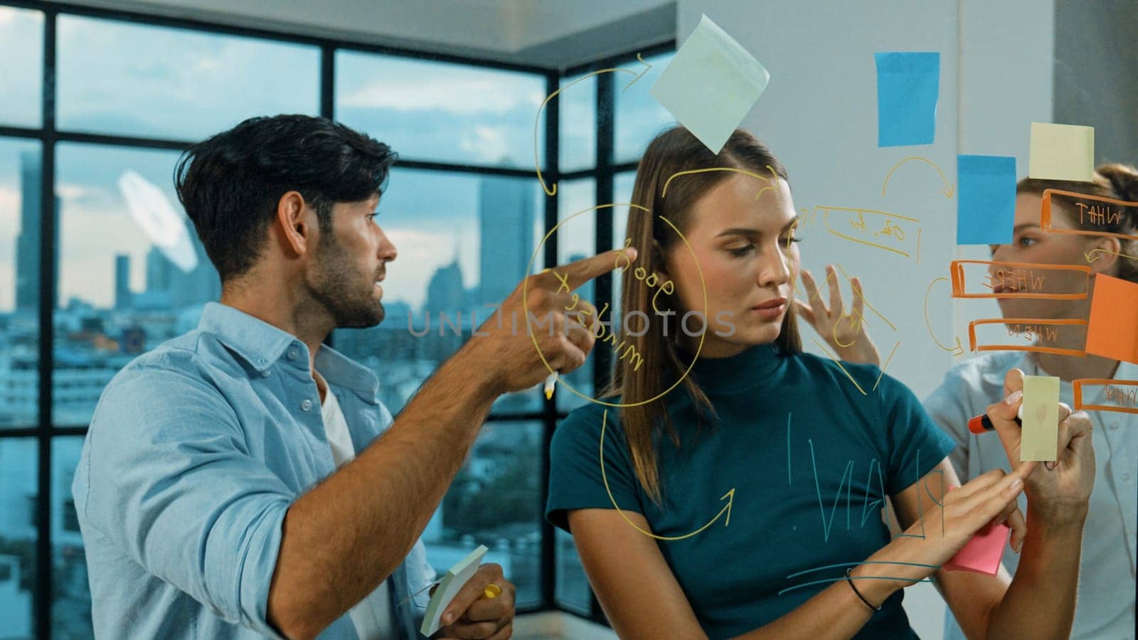 Professional business team brainstorm, sharing, thinking idea while skilled male leader write on sticky notes at glass wall. Skilled manager placed business plan on glass wall at office. Tracery