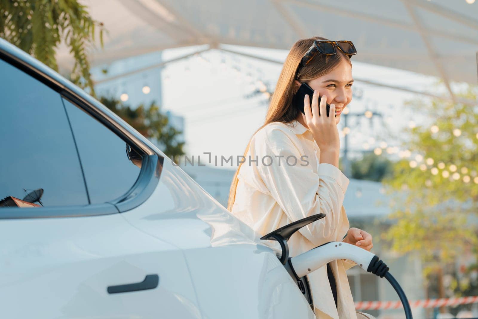 Sustainable urban commute with young woman pay electricity for EV electric car recharging at outdoor cafe in springtime garden, green city sustainability and environmental friendly EV car. Expedient