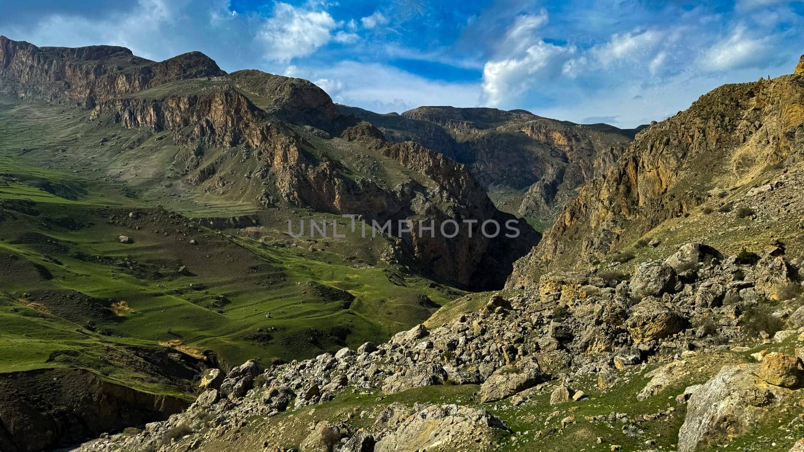 Mountain landscape with green valleys, rugged cliffs under blue sky with clouds. For advertising banner or post card of outdoor adventure and travel themes. by Lunnica