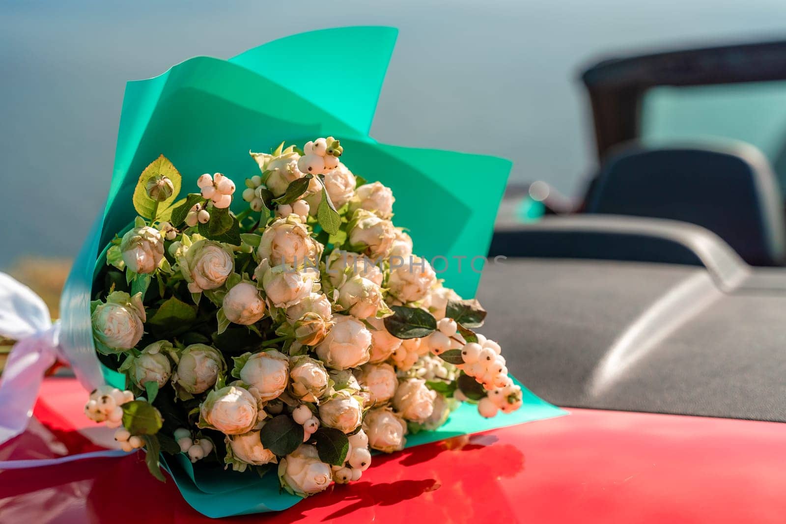 A bouquet of flowers is sitting on the hood of a red car. The flowers are white and red, and they are arranged in a vase. Concept of romance and love. by Matiunina