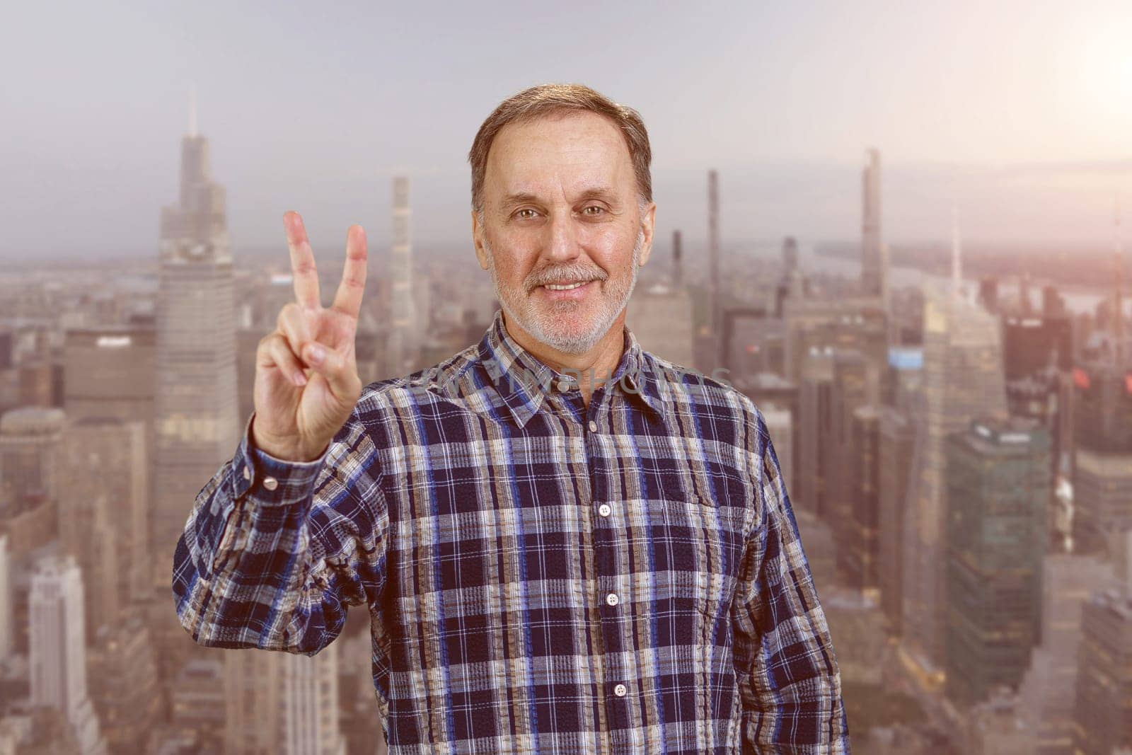 Happy confident mature man giving victory gesture sign. Urban cityscape background.