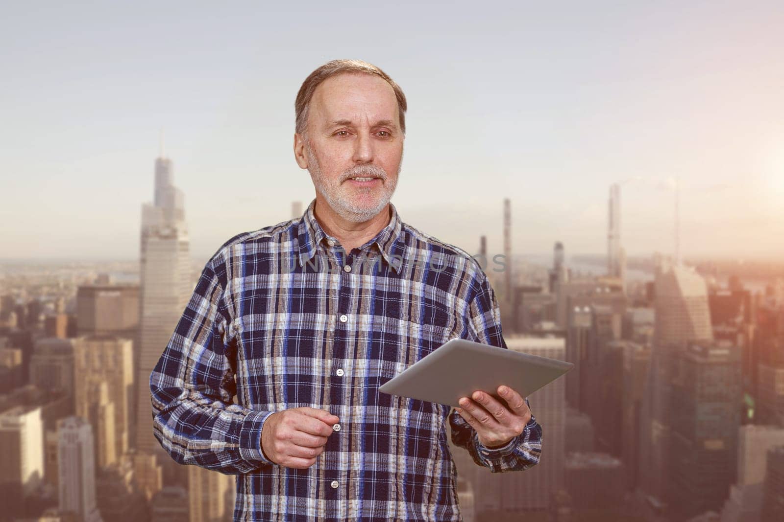 Portrait of aged elder man with tablet pc device. Evening cityscape background.