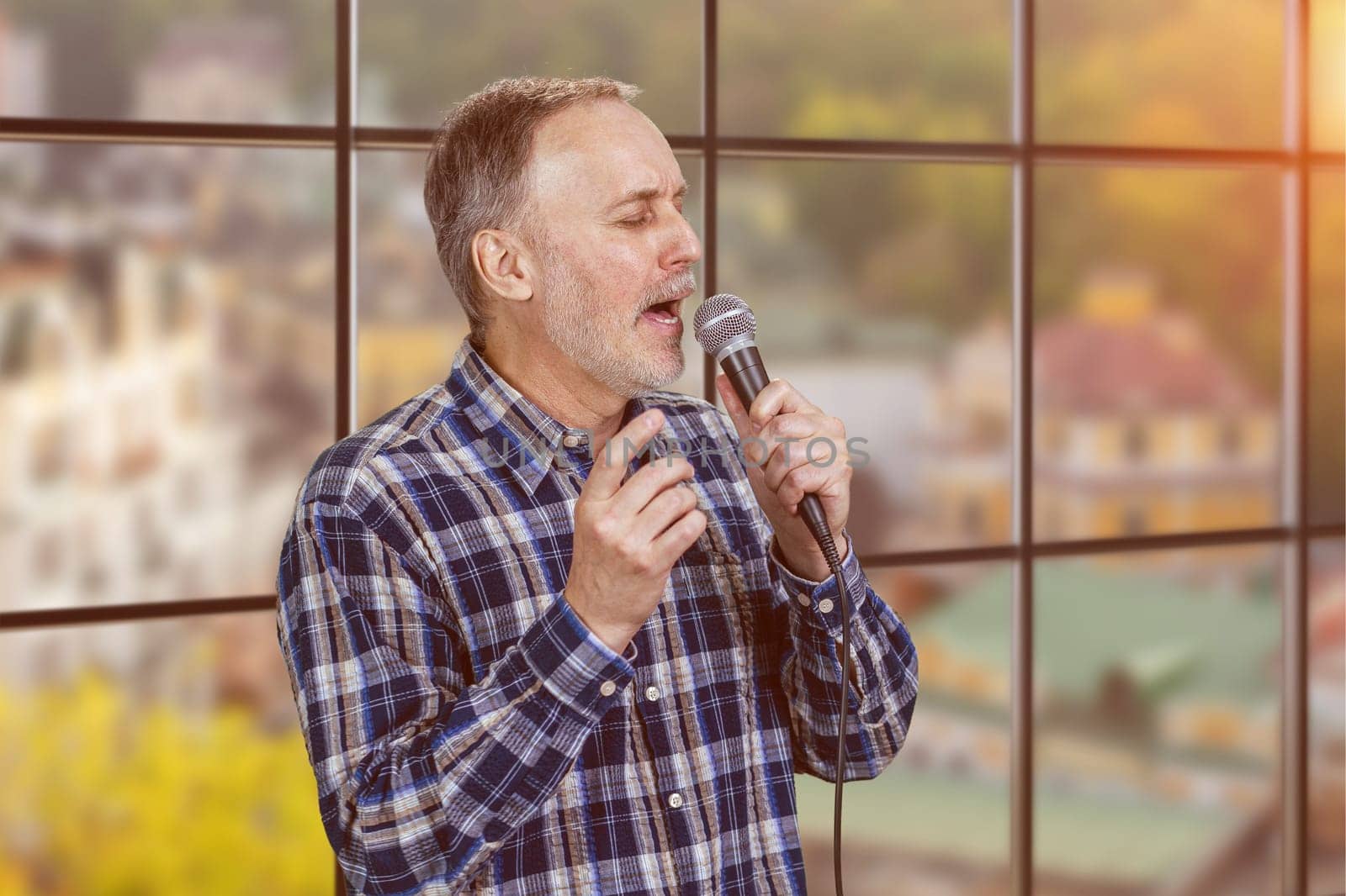 Expressive handsome mature man is singing in microphone. Checkered windows background.