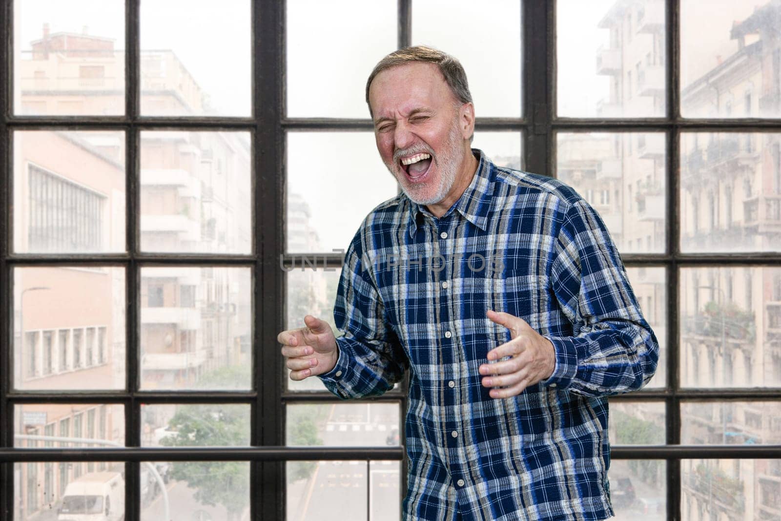 Handsome aged senior man smiling and laughing hard out loud because of funny joke. Standing indoors in office.