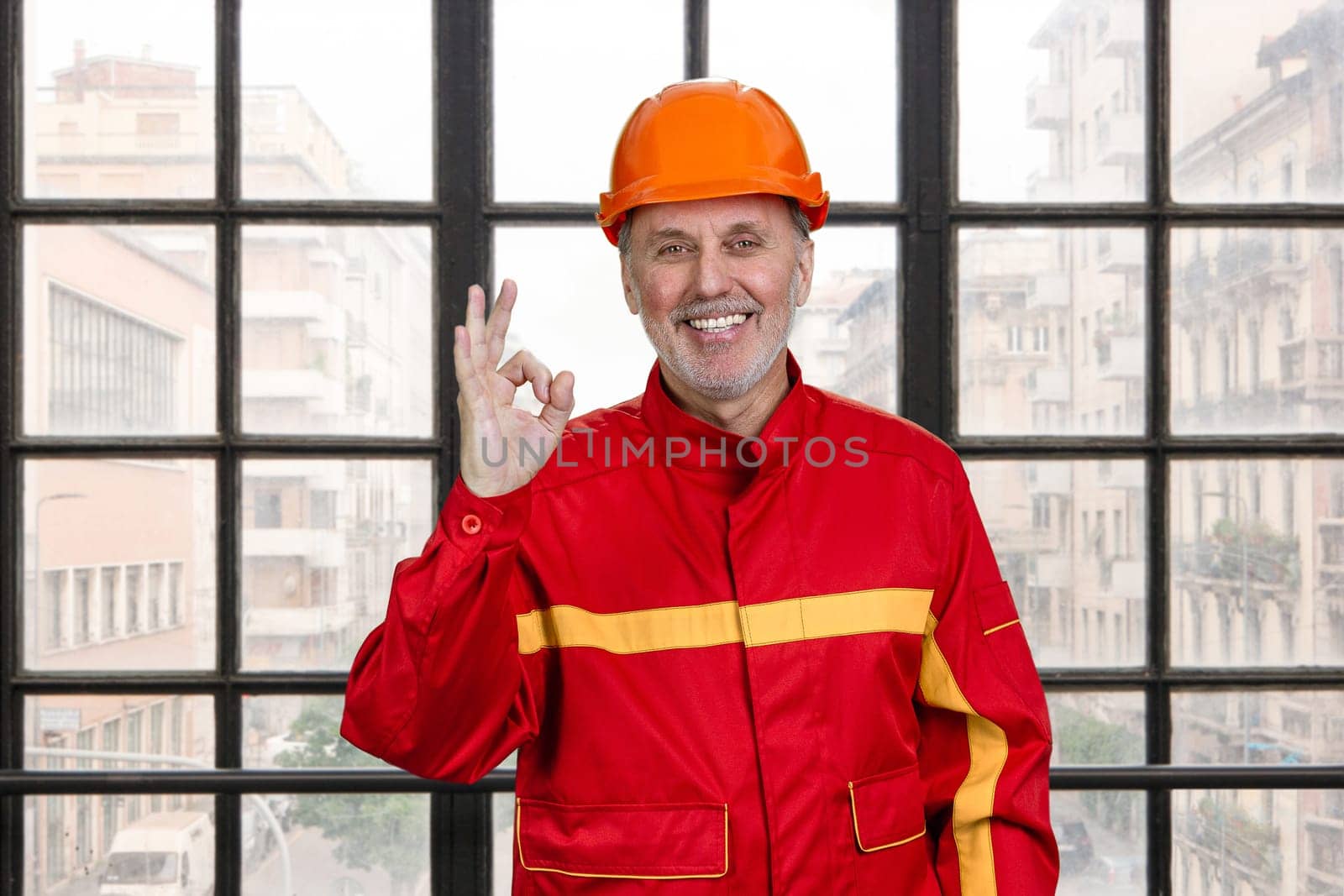 Smiling construction handyman worker in red uniform shows okay gesture sign. by super_picture
