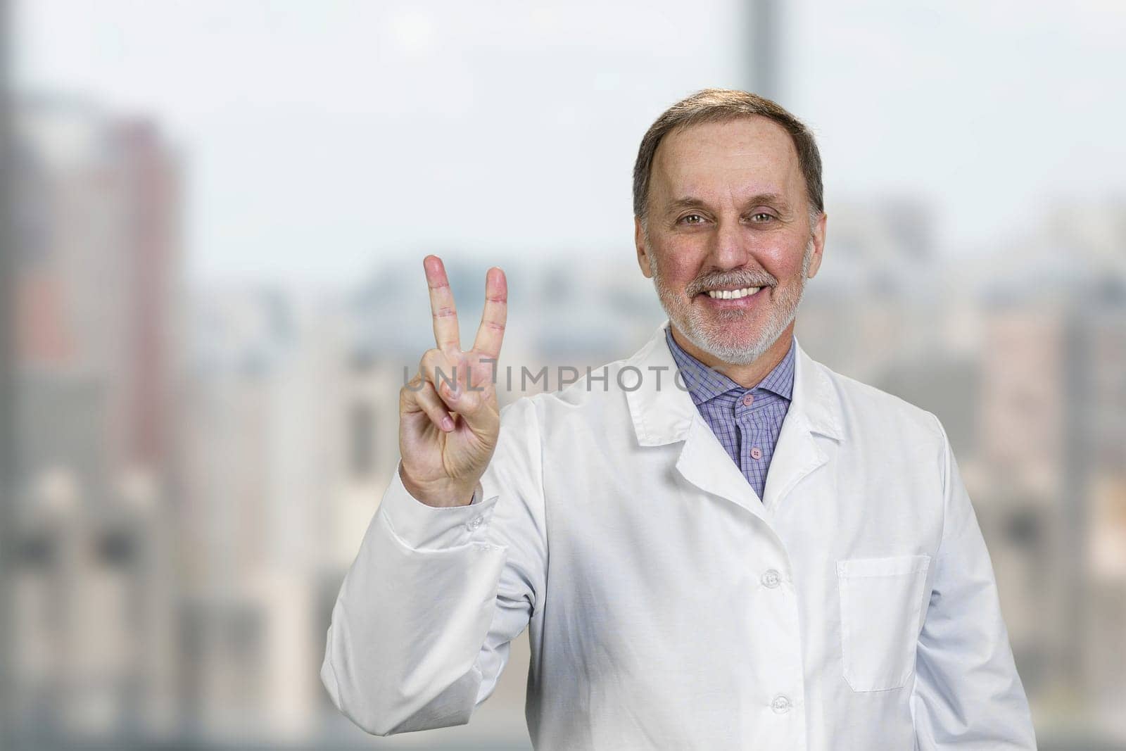 Cheerful senior caucasian doctor shows victory gesture sign. by super_picture