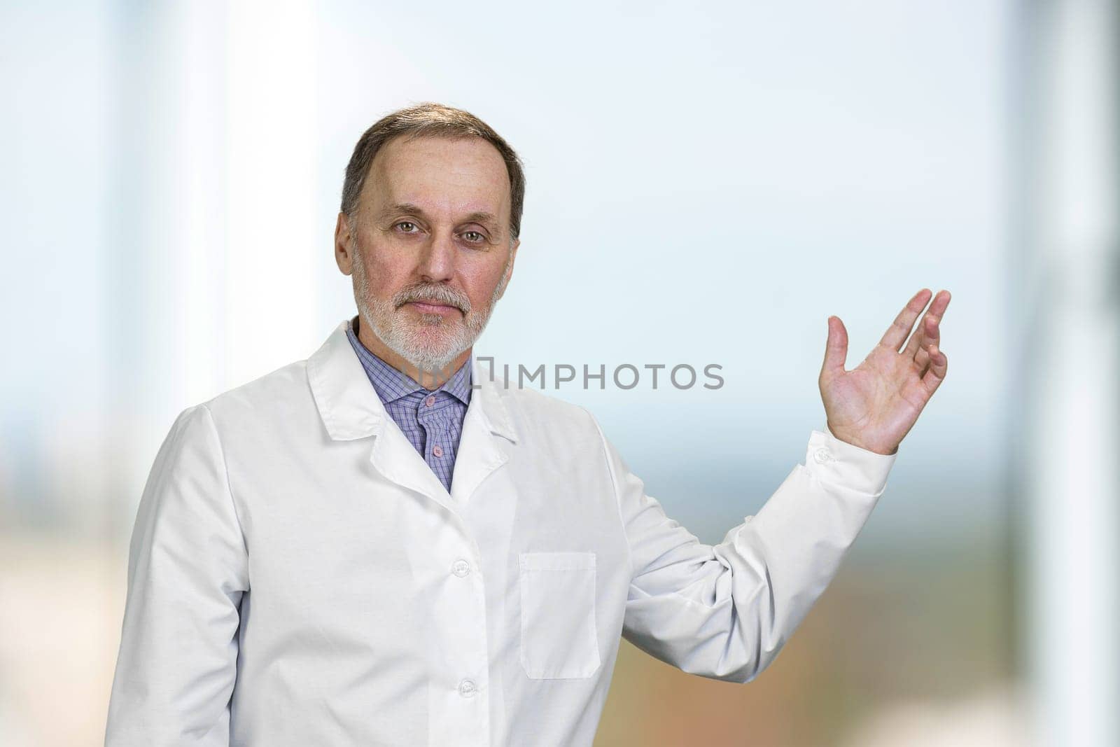 Portrait of senior doctor pointing up showing on copy space. Indoor blurred background.